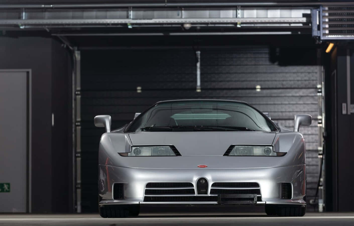 Bugatti Eb110 桌布 壁紙 — 一架流線型銀色Bugatti EB110 Super Sport停泊在昏暗的工業車庫中，頭頂有裸露的金屬橫樑。