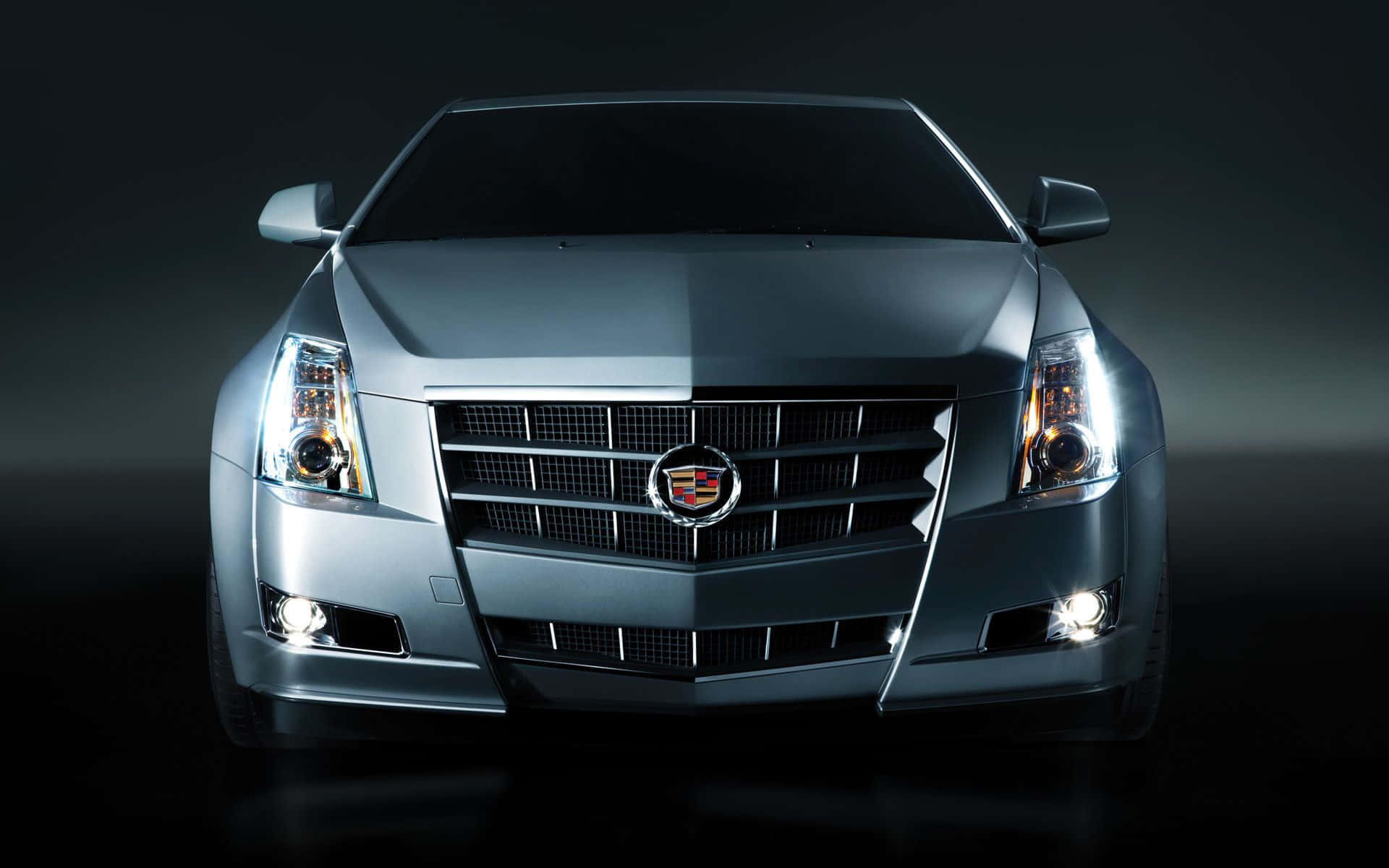 Cadillac Cts 桌布 壁紙 — 一輛時尚的銀色Cadillac ATS正面視圖，在黑暗的攝影棚背景下帶有發光的車頭燈。