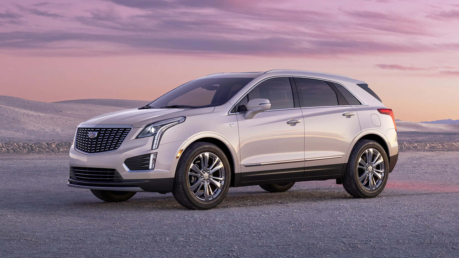 Cadillac Xt5 桌布 壁紙 — 一輛時尚的銀色凱迪拉克SUV停在碎石上，背景是柔和的粉紫色日落天空和連綿起伏的山丘。