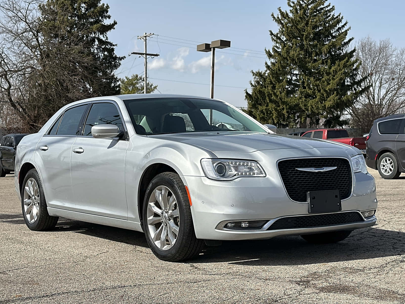 Chrysler 300 桌布 壁紙 — 一輛時尚的銀色Chrysler轎車停在裂開的瀝青路上，背景是明亮的藍天、散落的雲朵和常綠樹。