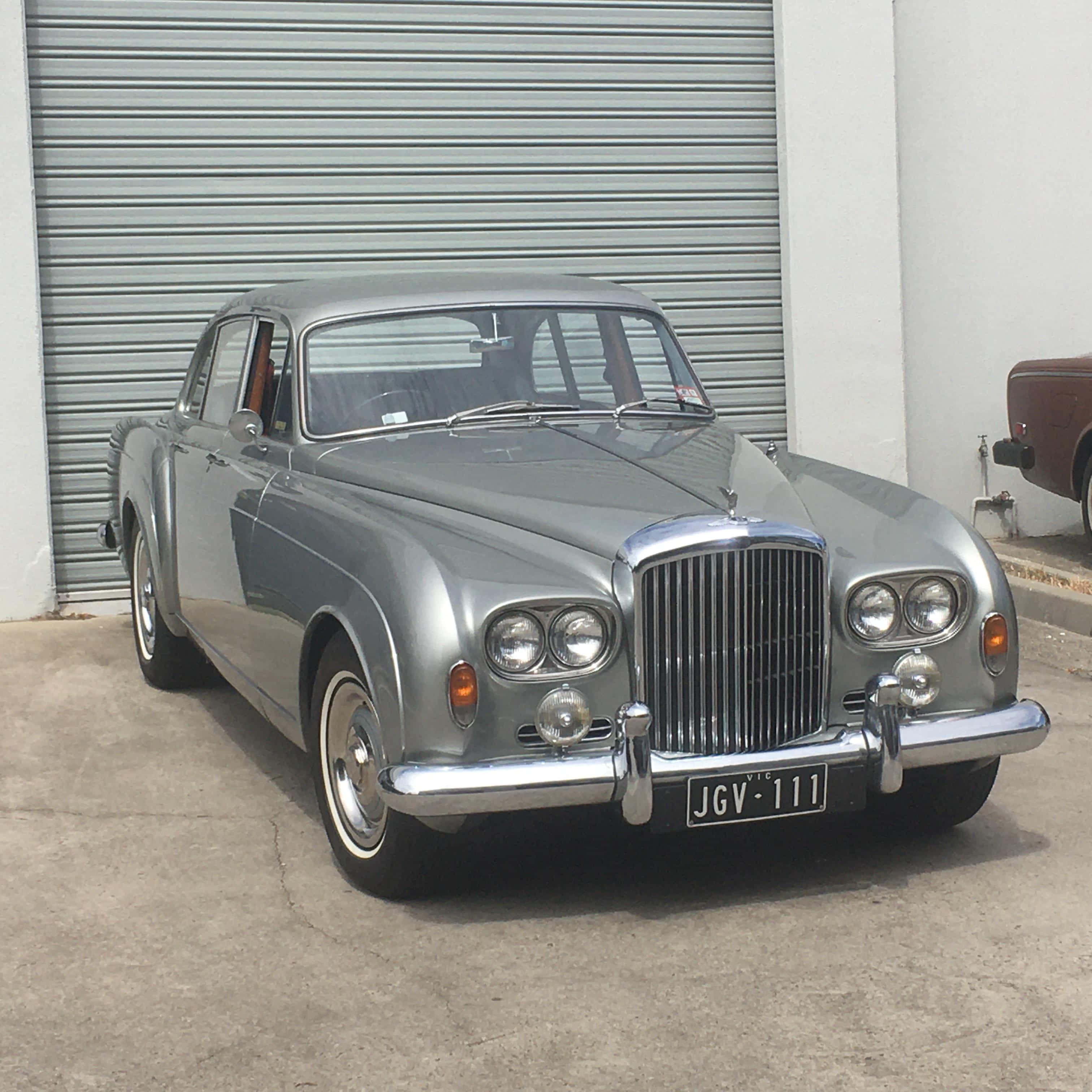 Bentley S3 桌布 壁紙 — 一架流線型銀色經典賓利房車停泊在混凝土車道上嘅波浪形金屬車庫門前。