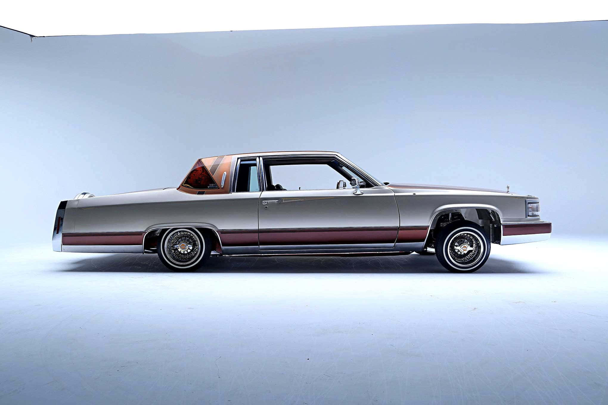 Cadillac Deville 桌布 壁紙 — 一架時尚的銀色經典汽車，帶有栗色飾邊和定制輪圈，站在極簡主義工作室中，背景是柔和的藍色漸變。