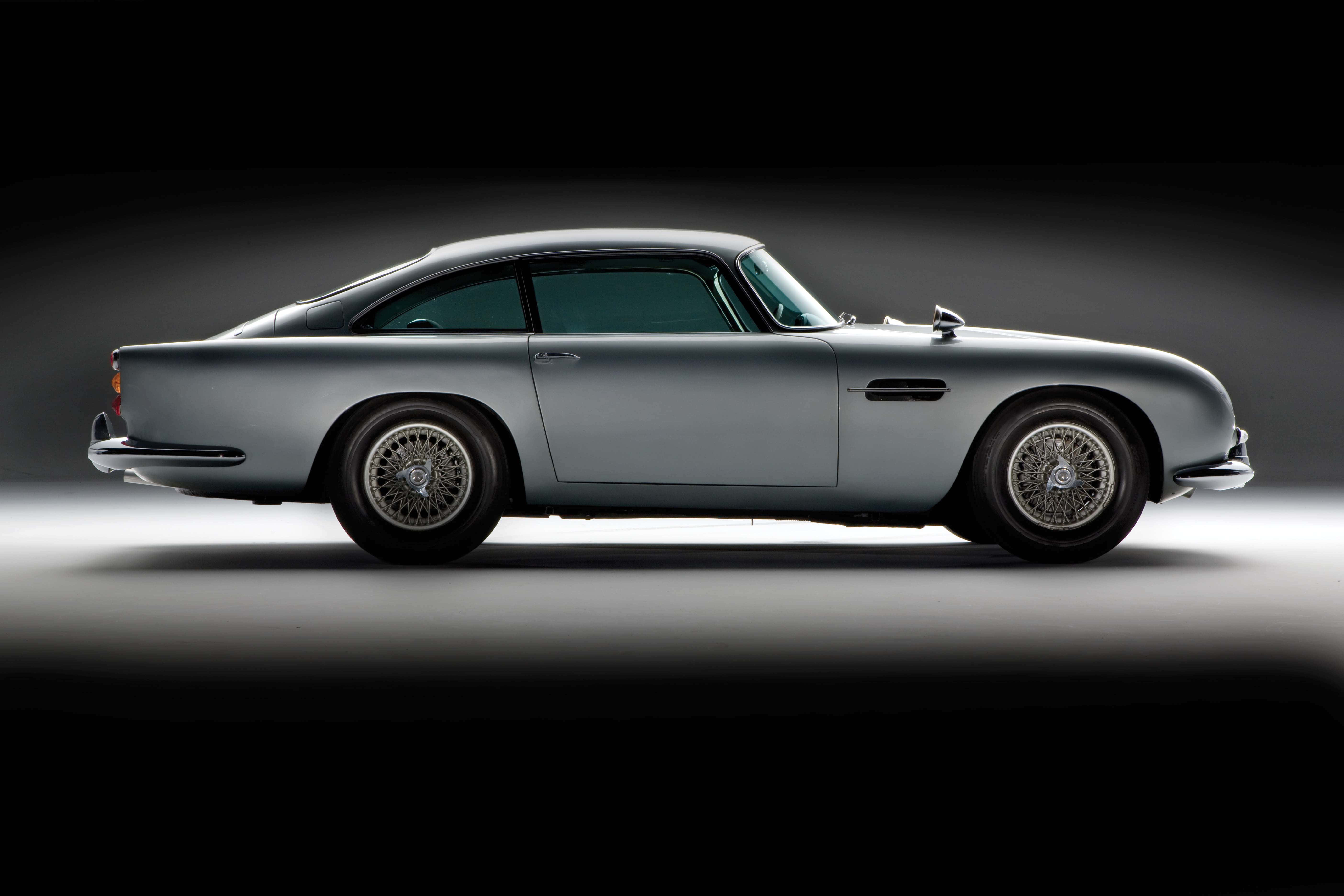 Aston Martin Db5 桌布 壁紙 — 一輛時尚的銀色經典跑車在戲劇性的攝影棚燈光下，在深色漸變背景中閃耀。