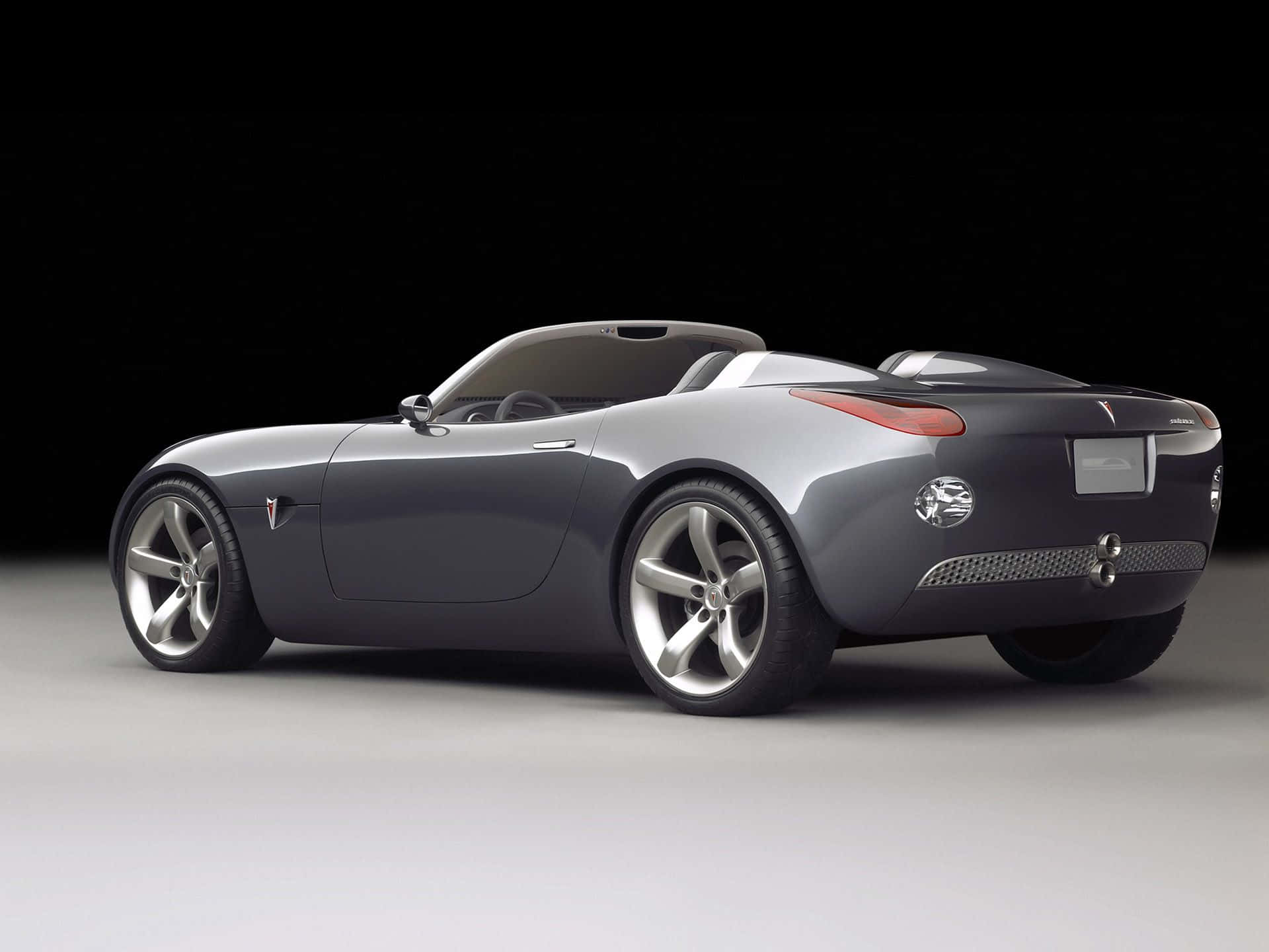 Pontiac Solstice 桌布 壁紙 — 時尚的銀色開篷跑車，採用極簡設計和紅色尾燈，在黑白工作室背景下展示。