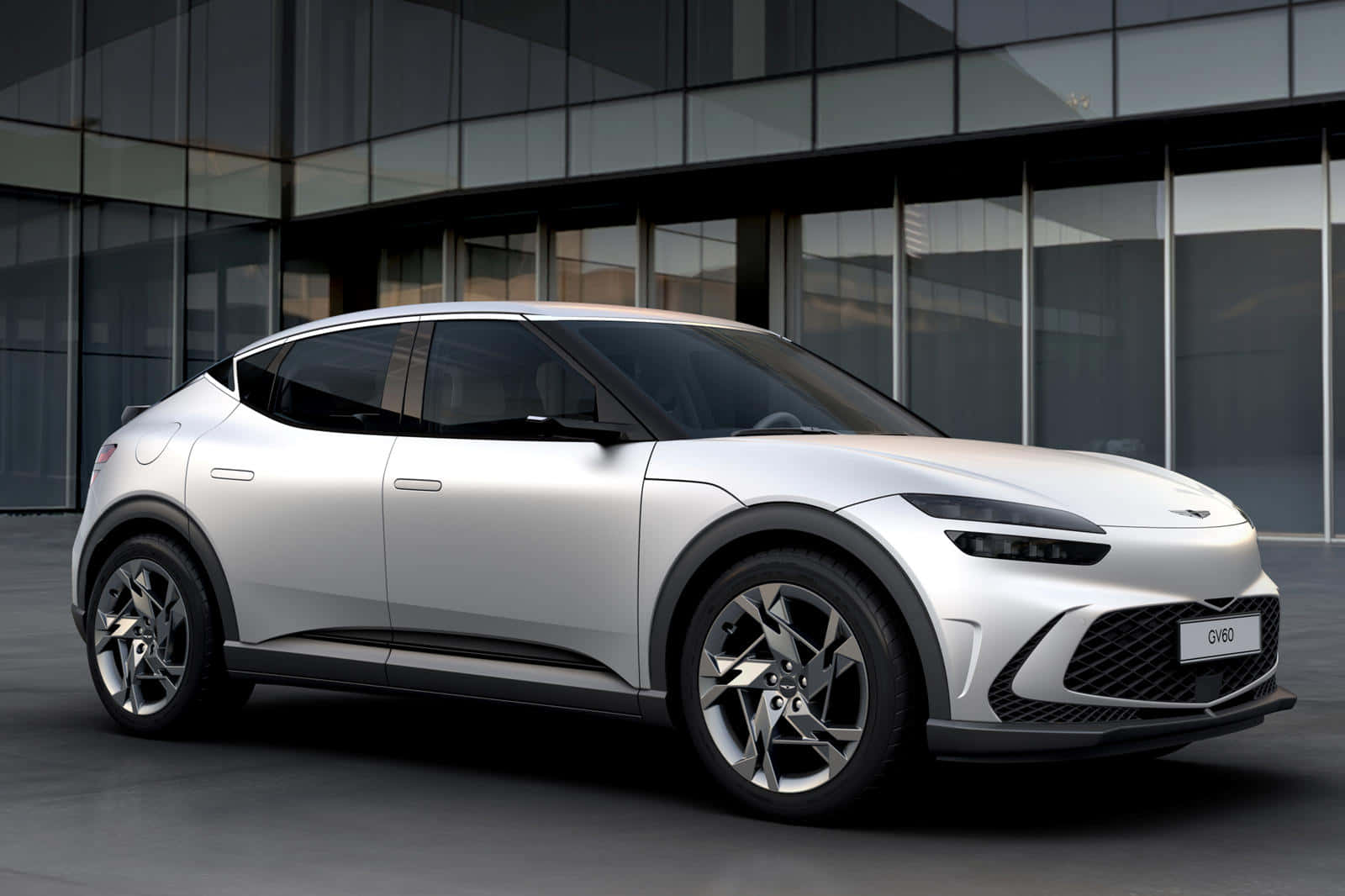 Genesis Gv60 桌布 壁紙 — 一輛時尚的銀色電動SUV停在一棟帶有反光窗戶的現代玻璃建築前。