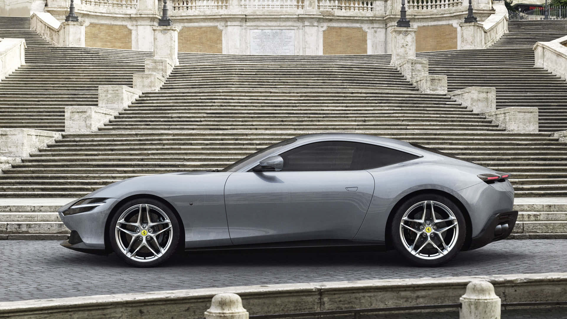 Ferrari Roma 桌布 壁紙 — 一輛時尚的銀色法拉利跑車停泊在陽光普照的城市廣場宏偉石階的底部。