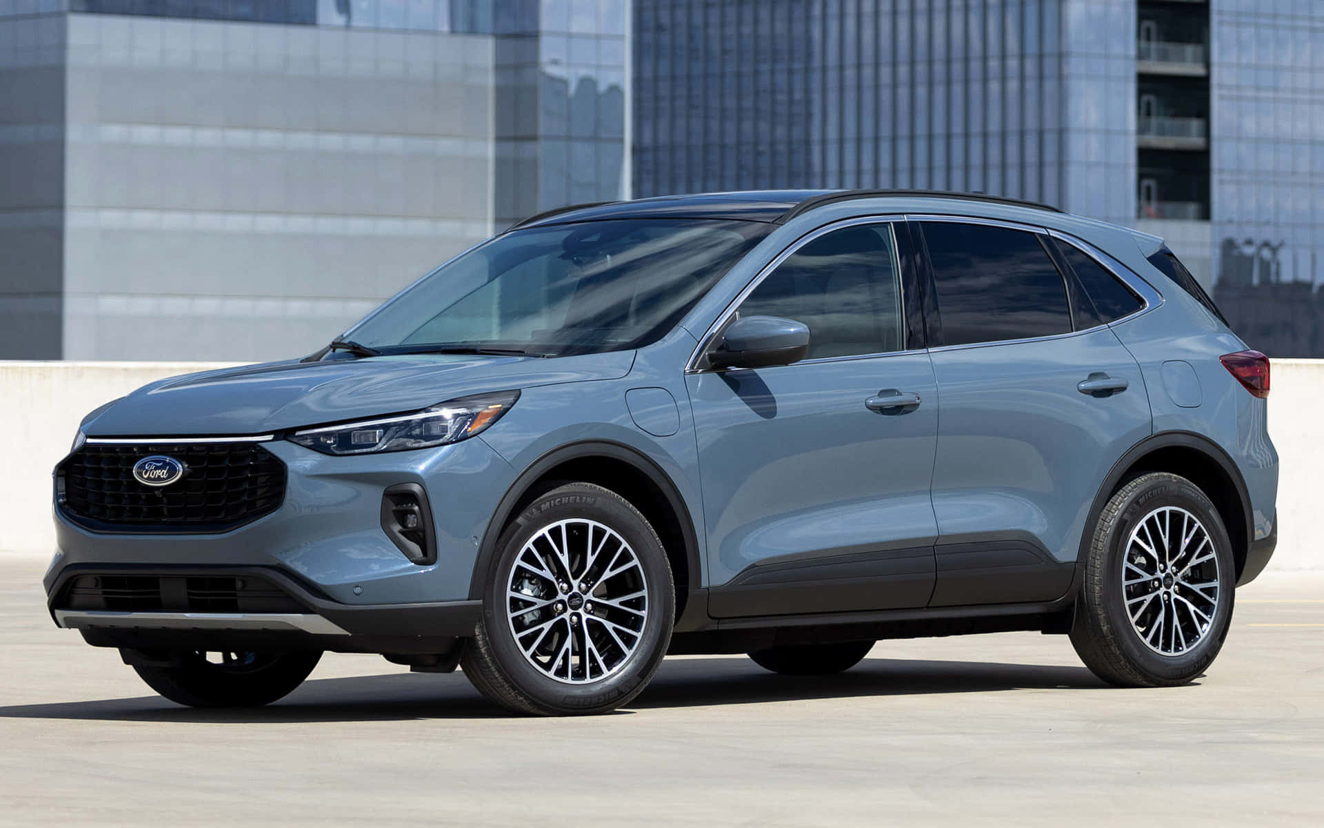 Ford Escape 桌布 壁紙 — 一架時尚的銀色福特電動SUV停泊在混凝土廣場上，背景是現代玻璃摩天大樓。