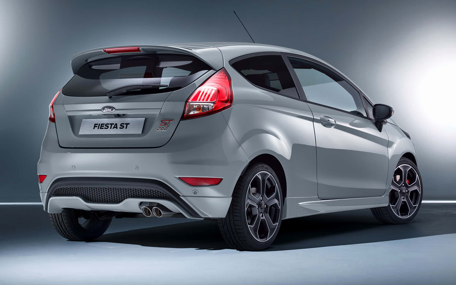 Ford Fiesta 桌布 壁紙 — 一輛時尚的銀色福特 Fiesta ST 跑車以後方四分之三角度展示，背景為漸變灰色工作室背景，配以戲劇性燈光。