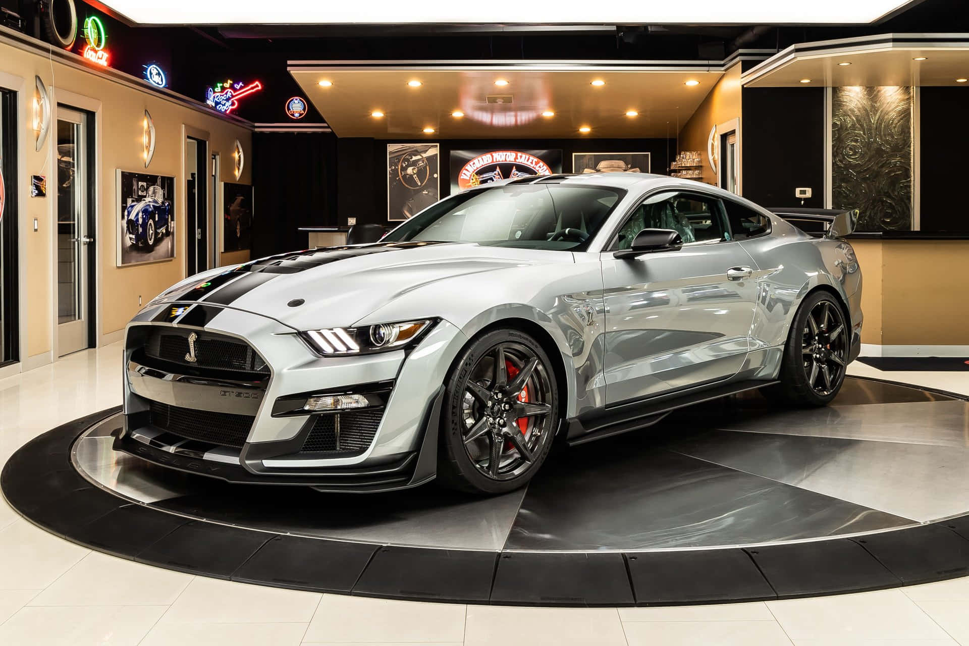  壁紙 — 一架時尚的銀色福特 Mustang GT 帶有黑色賽車條紋，位於現代汽車展廳的黑白格仔平台中央。