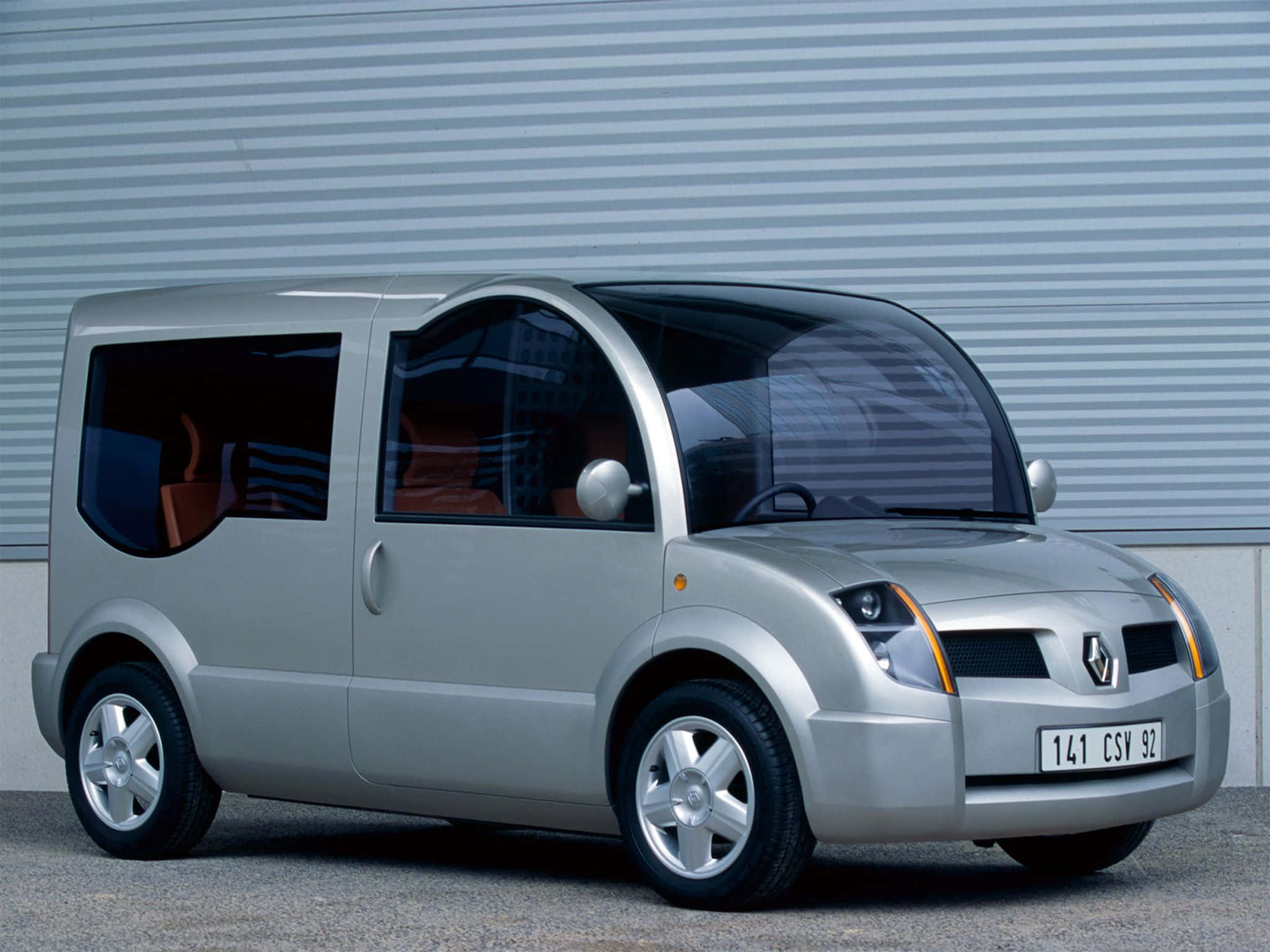 Renault Modus 桌布 壁紙 — 一輛時尚的銀色未來感廂型車，配有弧形玻璃窗，停靠在波紋金屬牆旁。