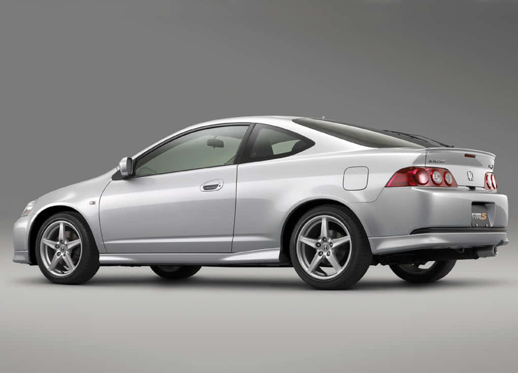 Honda Integra 桌布 壁紙 — 一輛流線型銀色本田轎跑車，帶紅色尾燈，側面展示在灰色中性攝影棚背景前。