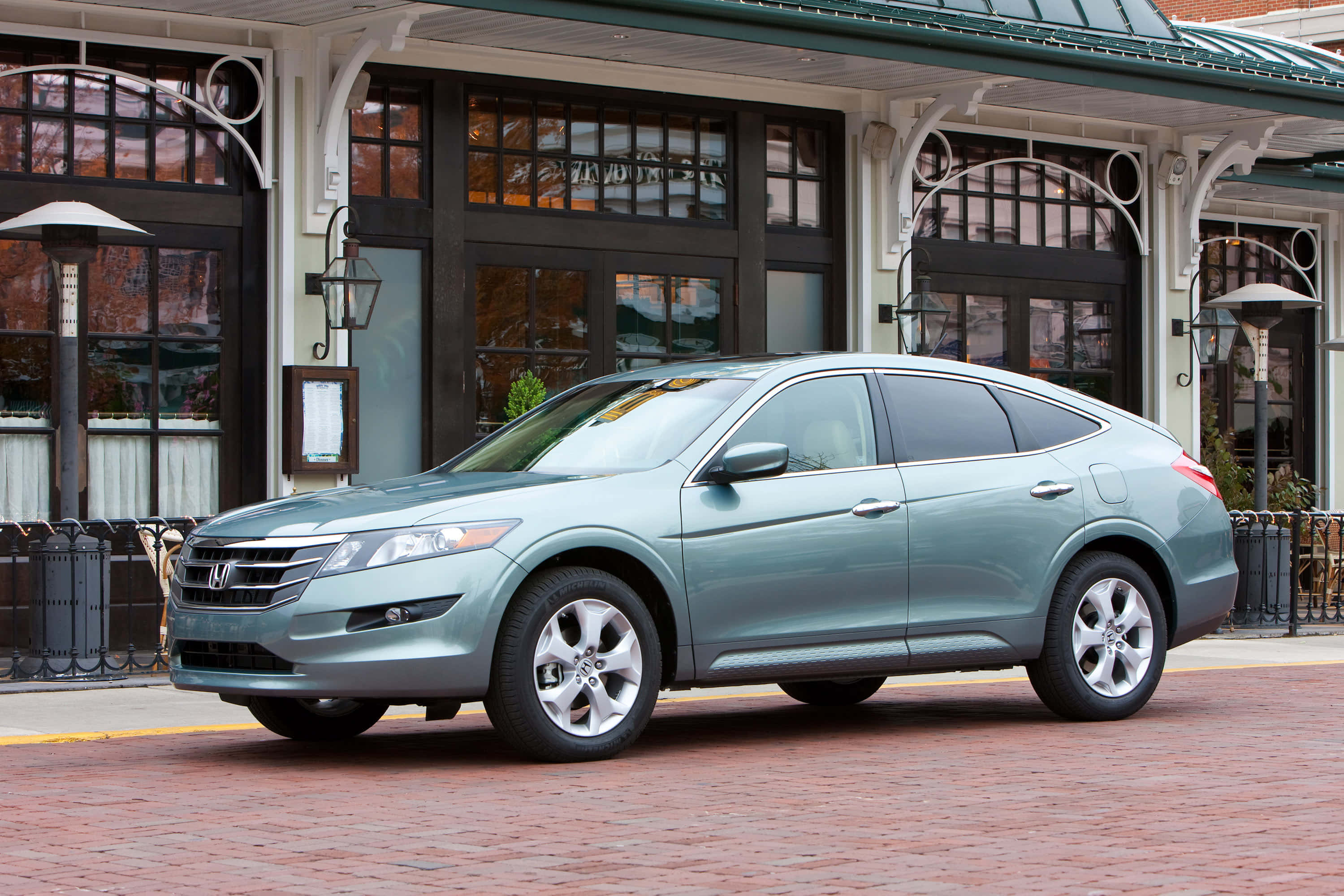 Honda Crosstour 桌布 壁紙 — 一架時尚的銀色本田 Crosstour 停在紅磚街上，前面是經典的店鋪，有拱形窗戶和復古燈籠。