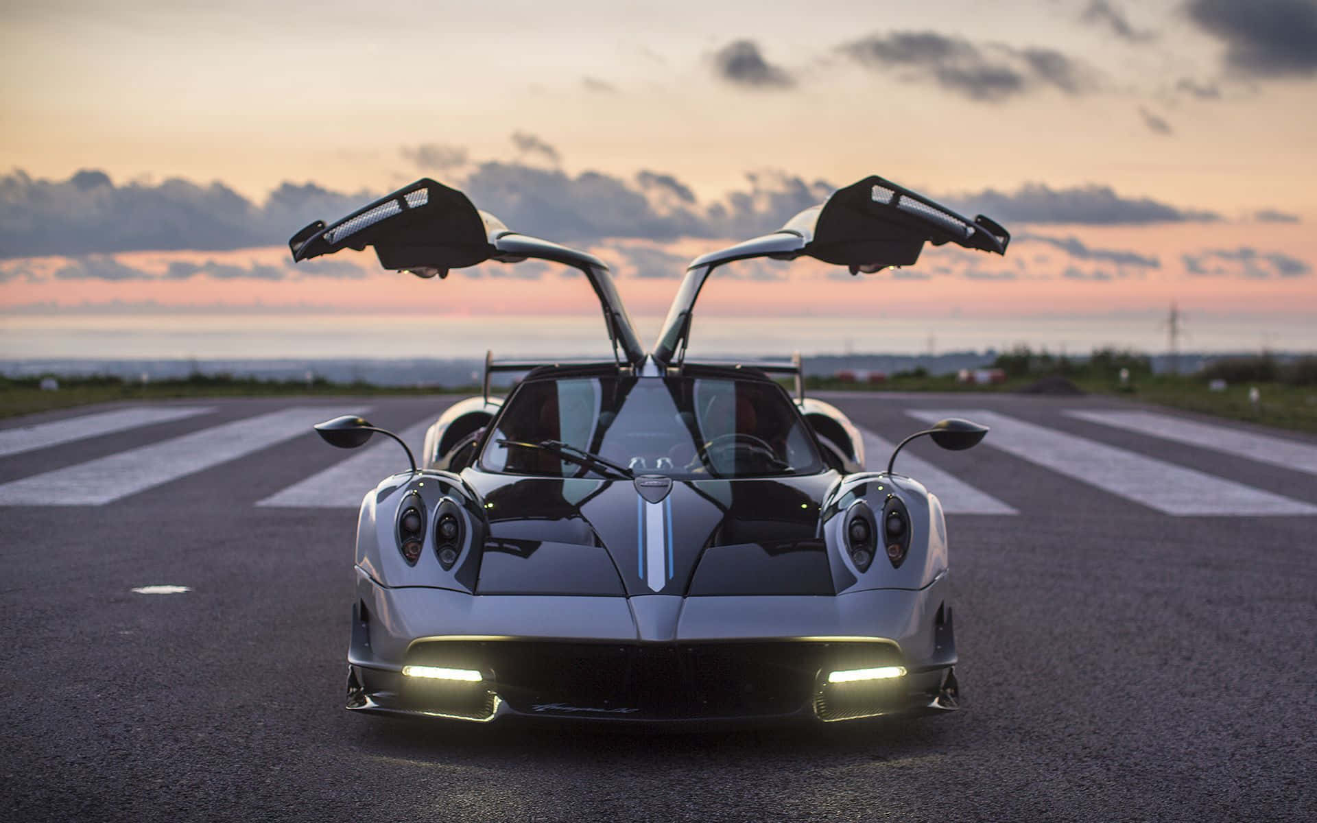 Pagani Huayra Roadster Bc 桌布 壁紙 — 一架時尚的銀色超級跑車，鷗翼車門打開，停在日落時分的跑道上，天空呈現粉紅色和橙色。