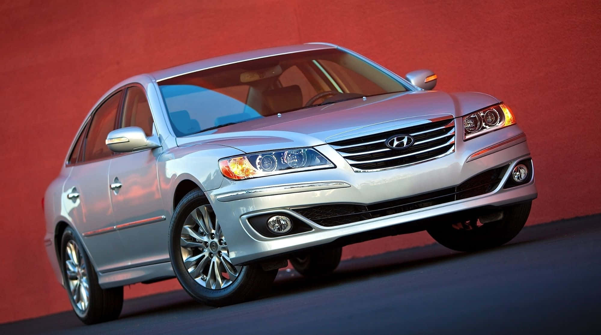 Hyundai Azera 桌布 壁紙 — 一輛時尚的銀色現代房車在攝影棚燈光下，映襯著鮮紅色的牆壁閃閃發光。