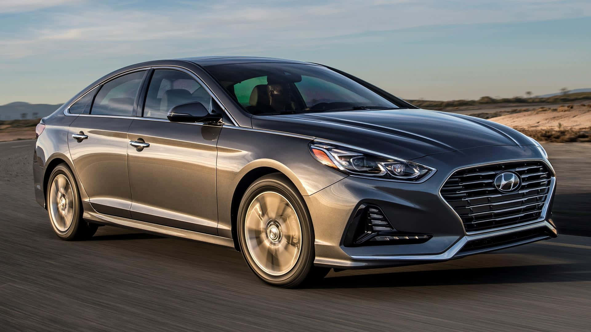 Hyundai Sonata 桌布 壁紙 — 一輛流線型銀色現代索納塔在晴朗藍天和遠山背景下，沿沙漠公路飛馳。