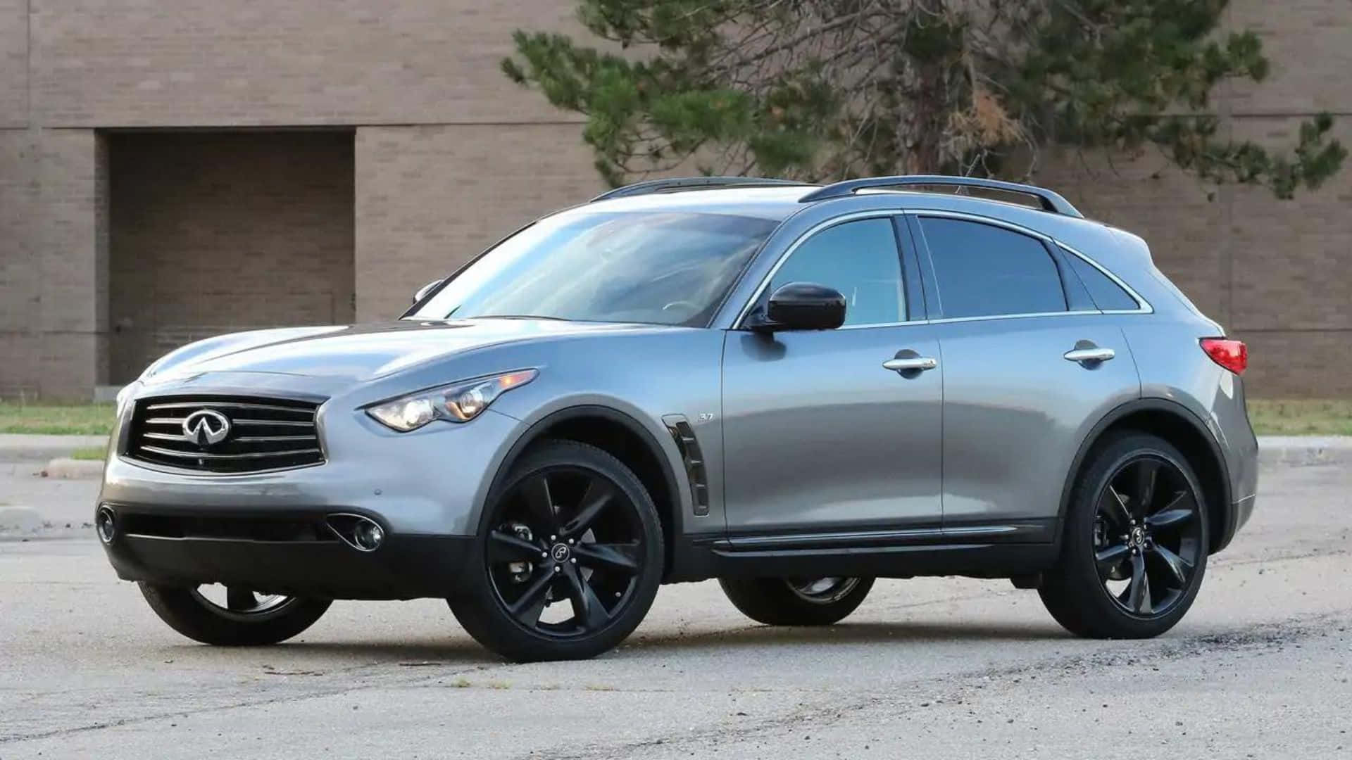 Infiniti Qx70 桌布 壁紙 — 一輛時尚的銀色Infiniti QX70 SUV，配備黑色輪圈，停在磚砌建築前的瀝青路面上，周圍有樹木。