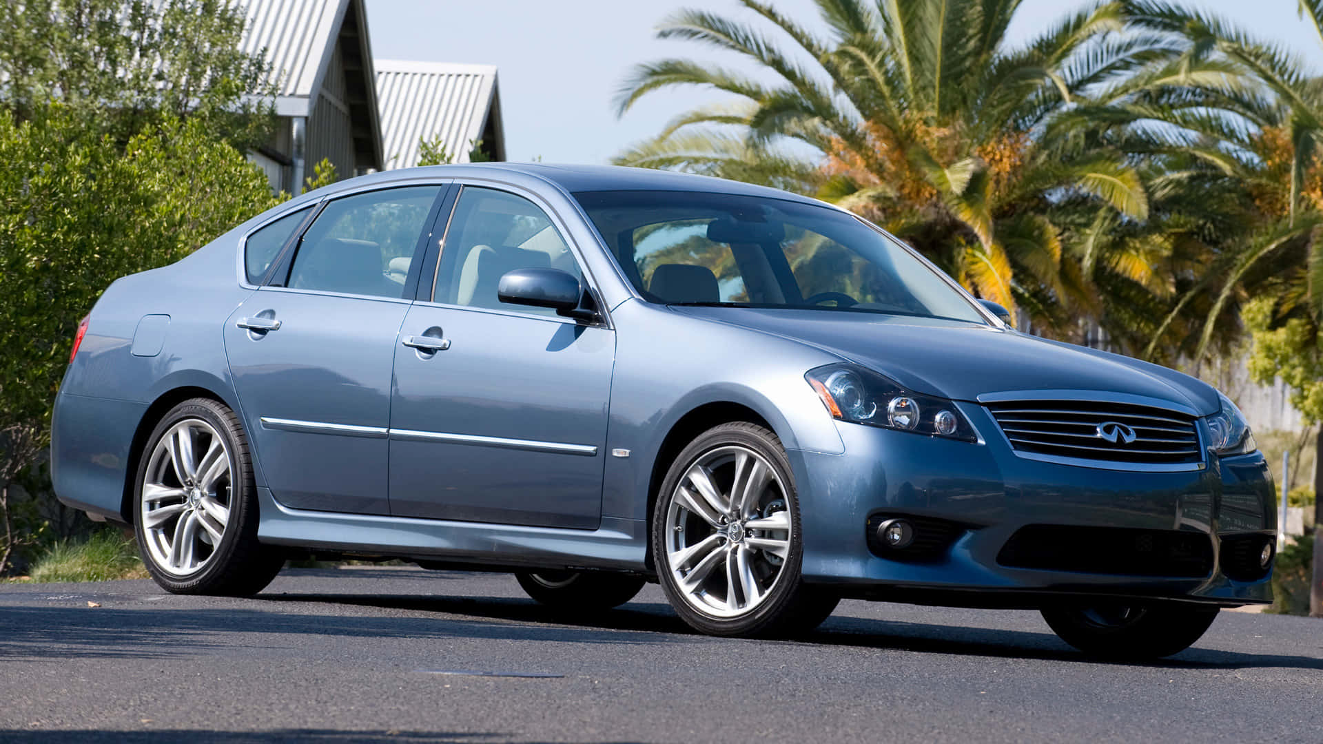Infiniti M35 桌布 壁紙 — 一輛時尚的銀色Infiniti房車停在瀝青路上，背景有棕櫚樹和房屋，在明亮的日光下。