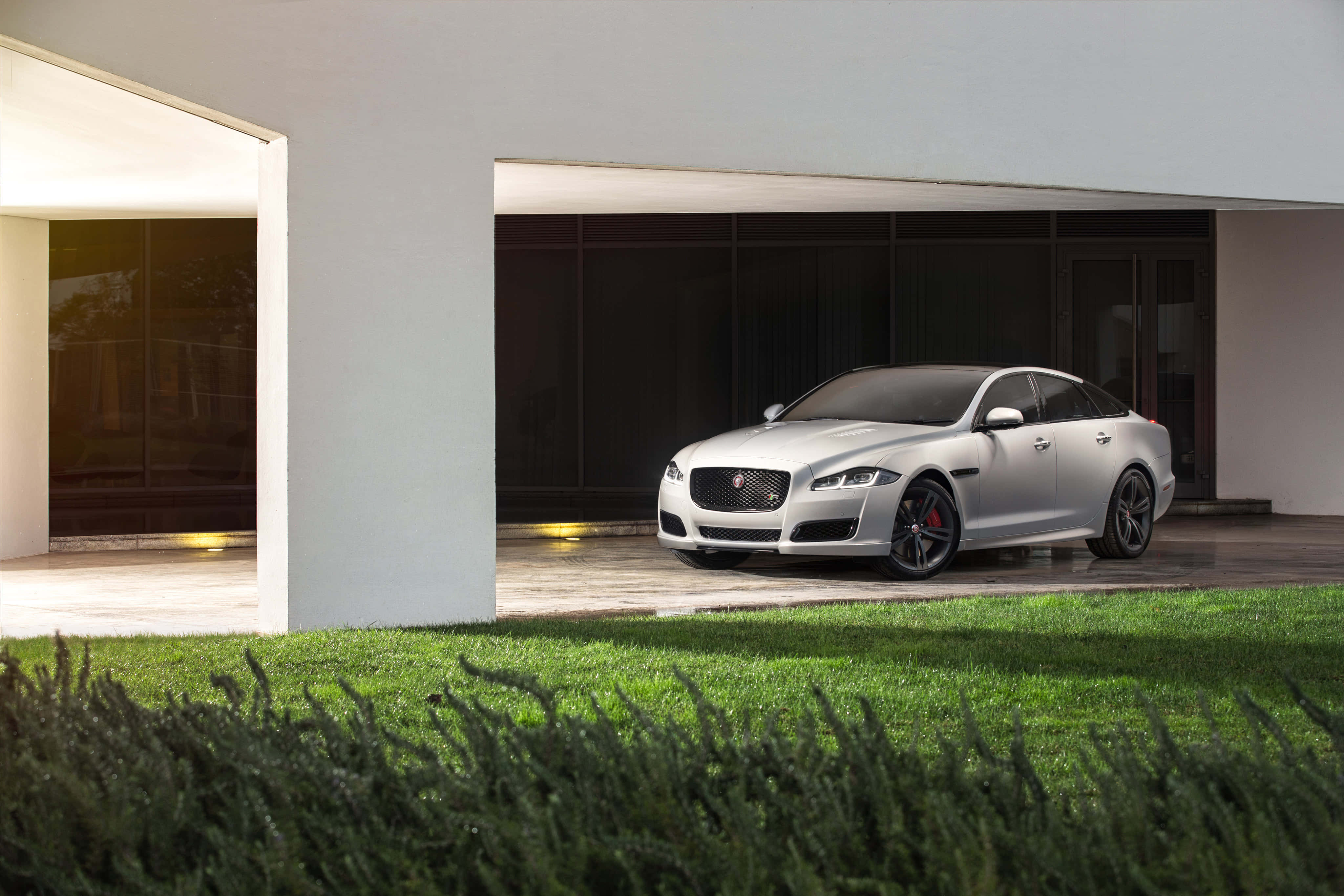Jaguar Xjr 桌布 壁紙 — 一輛時尚的銀色積架XF停泊在現代白色房屋下，房屋有玻璃門和前景的綠色草地。