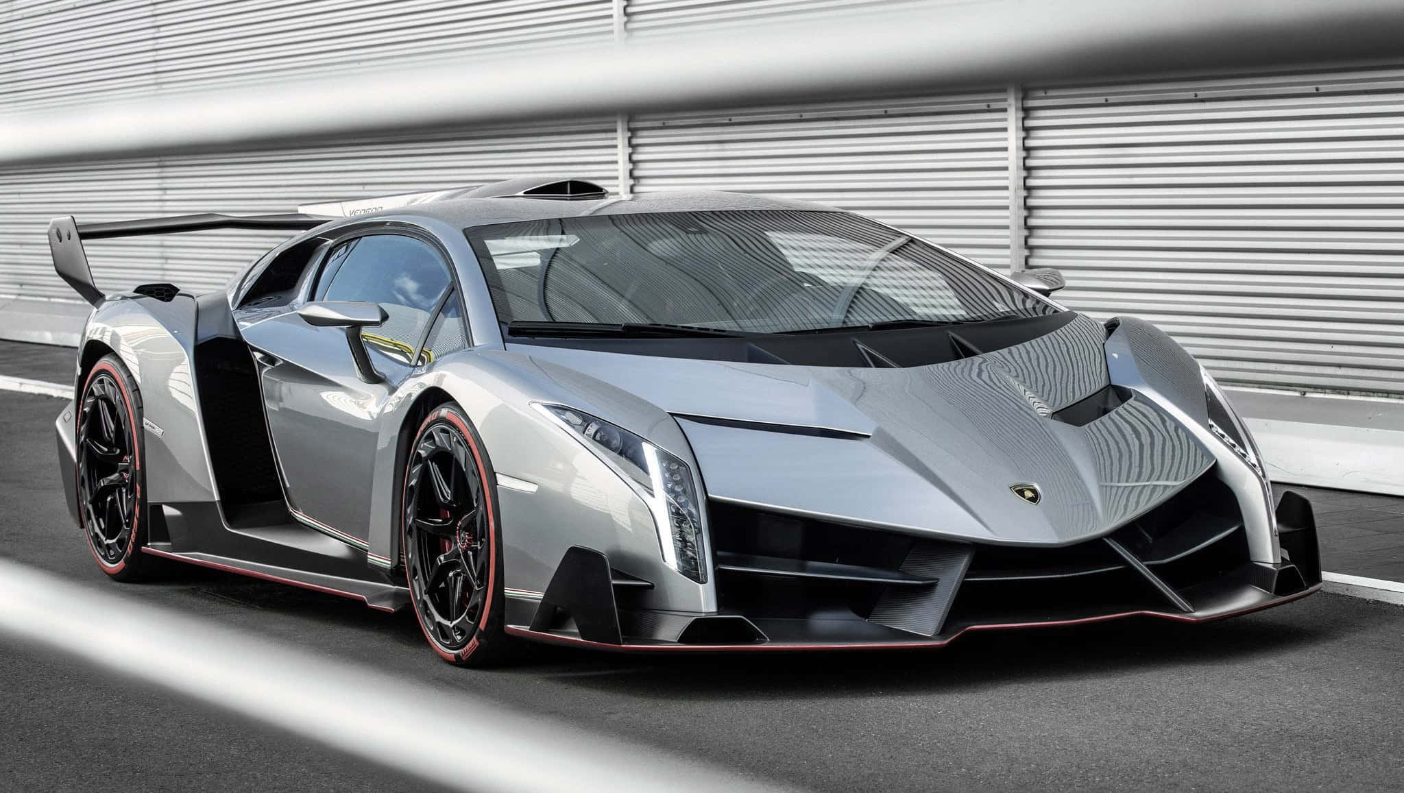 Lamborghini Veneno 桌布 壁紙 — 一輛時尚的銀色林寶堅尼 Veneno 帶有紅色點綴，停泊在賽車場上，背景是波紋金屬牆。