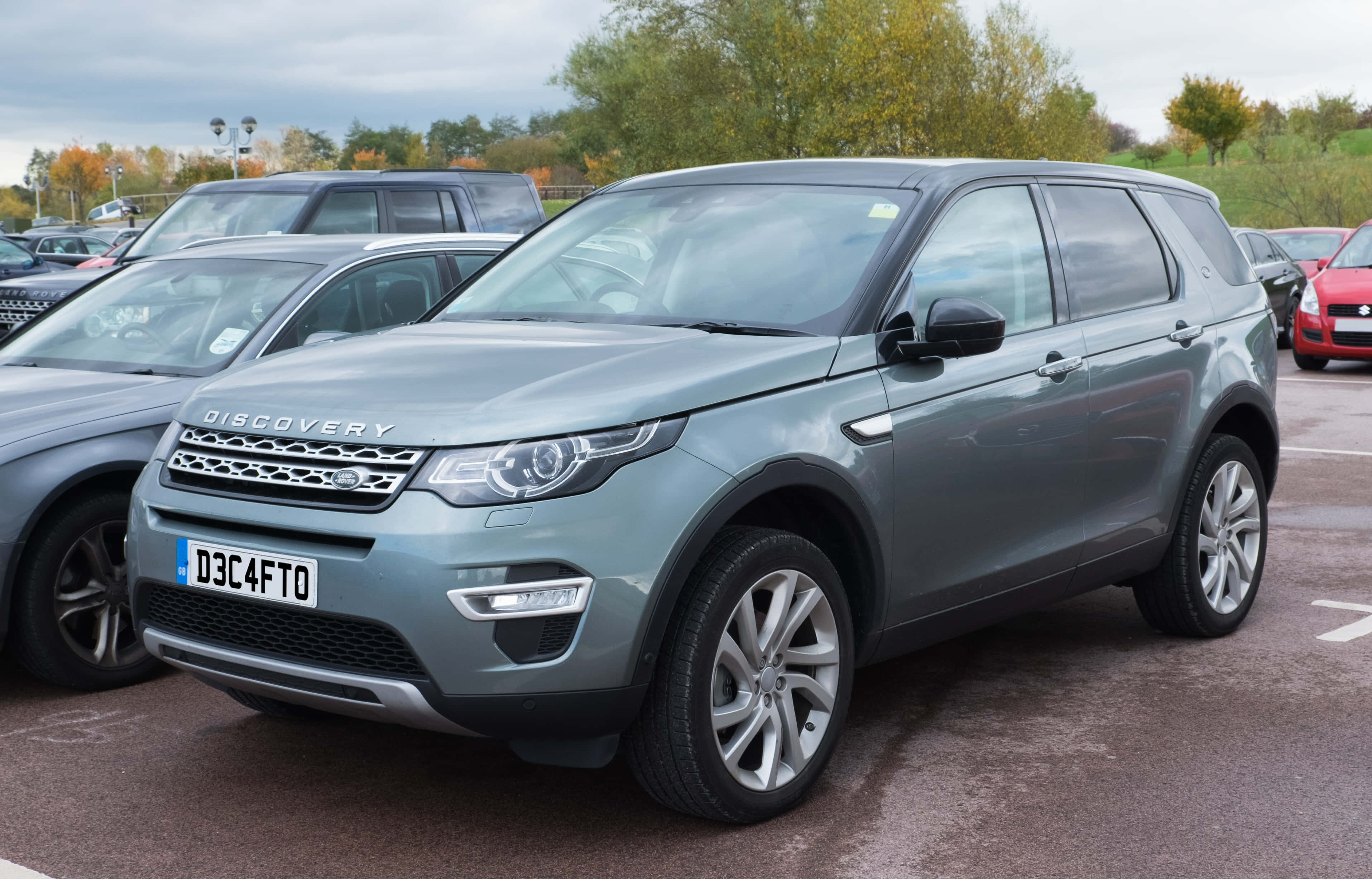 Land Rover Discovery 桌布 壁紙 — 一輛時尚的銀色 Land Rover Discovery SUV 停泊在停車場，背景有秋樹和陰天。