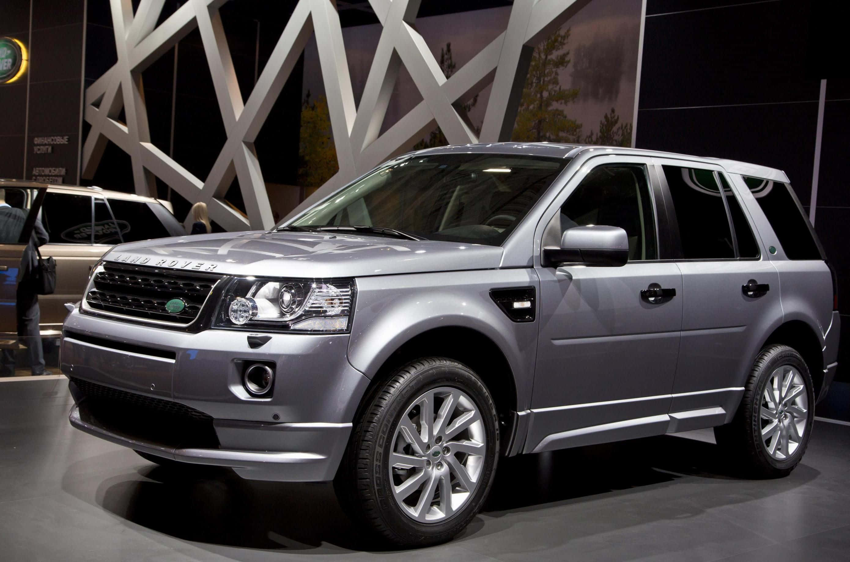 Land Rover Freelander 桌布 壁紙 — 一輛時尚的銀色Land Rover SUV在明亮的燈光下於車展中閃耀，背景為幾何白色。