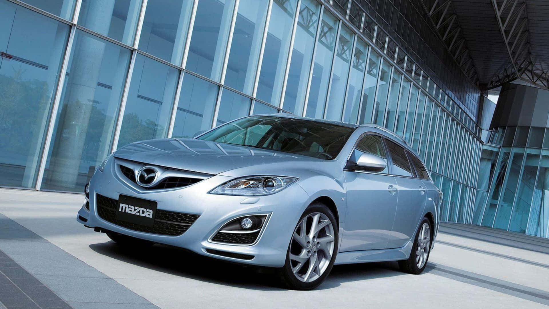 Mazda 6 桌布 壁紙 — 一架時尚的銀色萬事得旅行車停泊在現代玻璃建築前，在明亮的日光下。