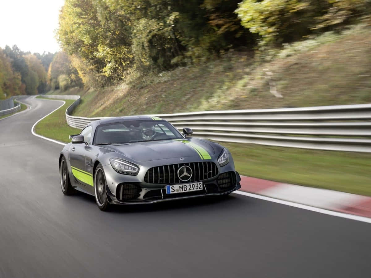  壁紙 — 一輛時尚的銀色 Mercedes-AMG GT R 帶有螢光綠色條紋，沿著蜿蜒的秋季森林道路行駛。