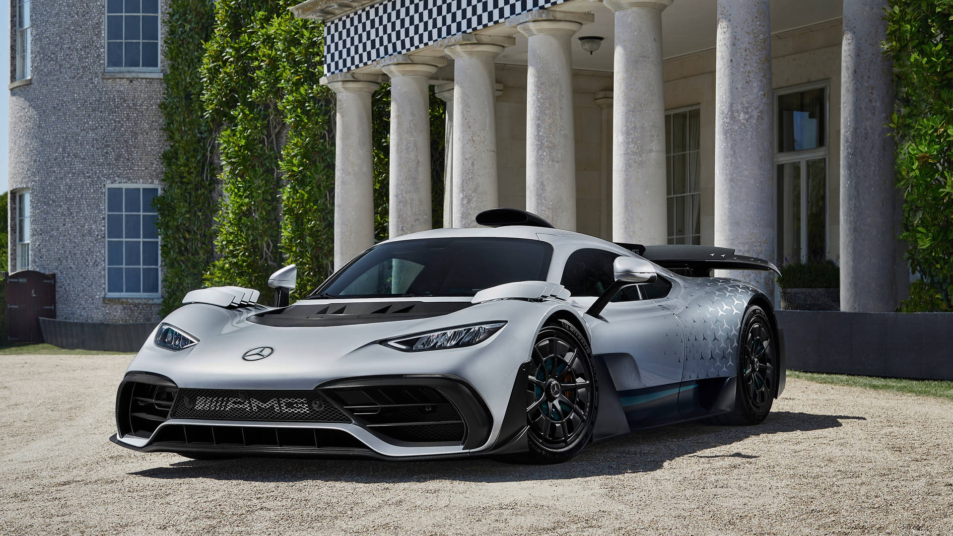 銀色Mercedes-AMG One hypercar停泊在一座有柱廊和常春藤的宏偉石造大宅前。