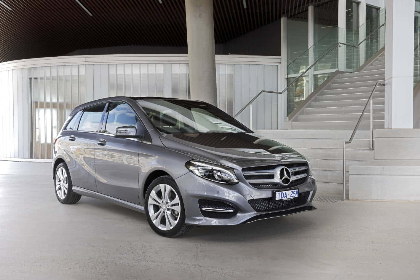 Mercedes Benz B-class 桌布 壁紙 — 一輛時尚的銀色 Mercedes-Benz B-Class 旅行車停泊在現代建築結構下，該結構設有混凝土樓梯和玻璃欄杆。