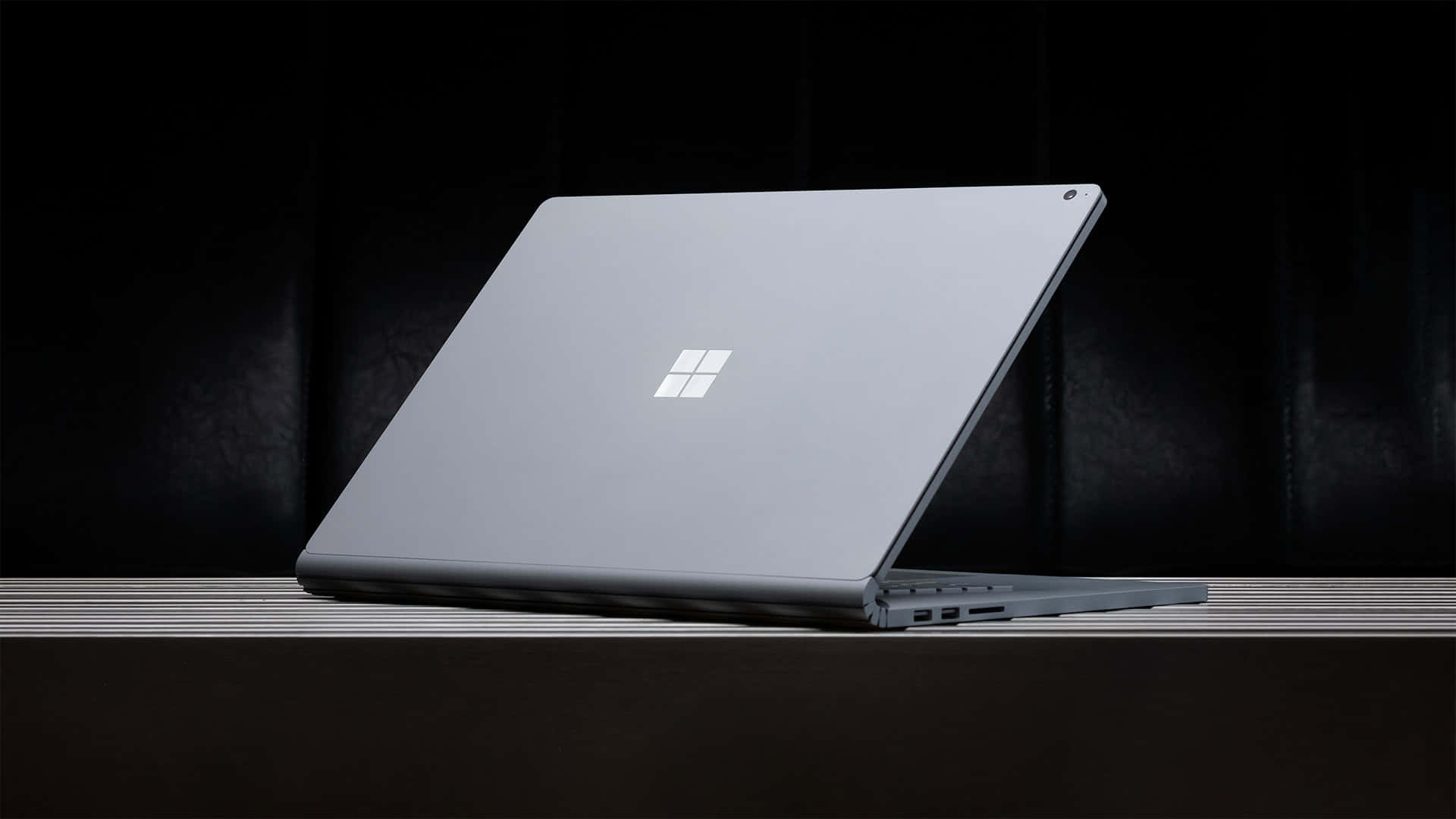  壁紙 — 一部時尚的銀色 Microsoft Surface 手提電腦打開放在木質表面上，背景為深色紋理。