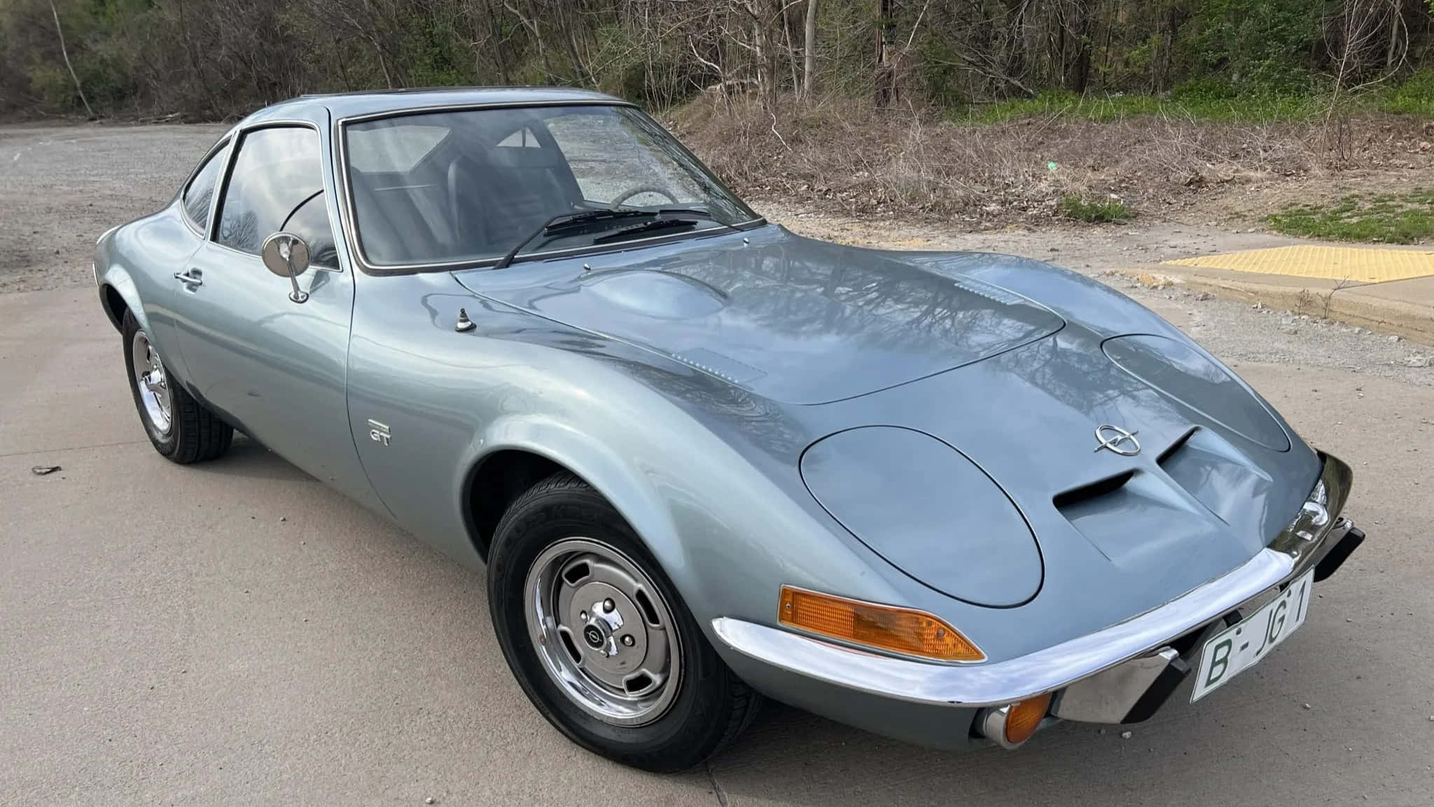 Opel Gt 桌布 壁紙 — 一架時尚的銀色歐寶GT跑車停泊在混凝土場地上，背景有乾燥灌木和樹木。