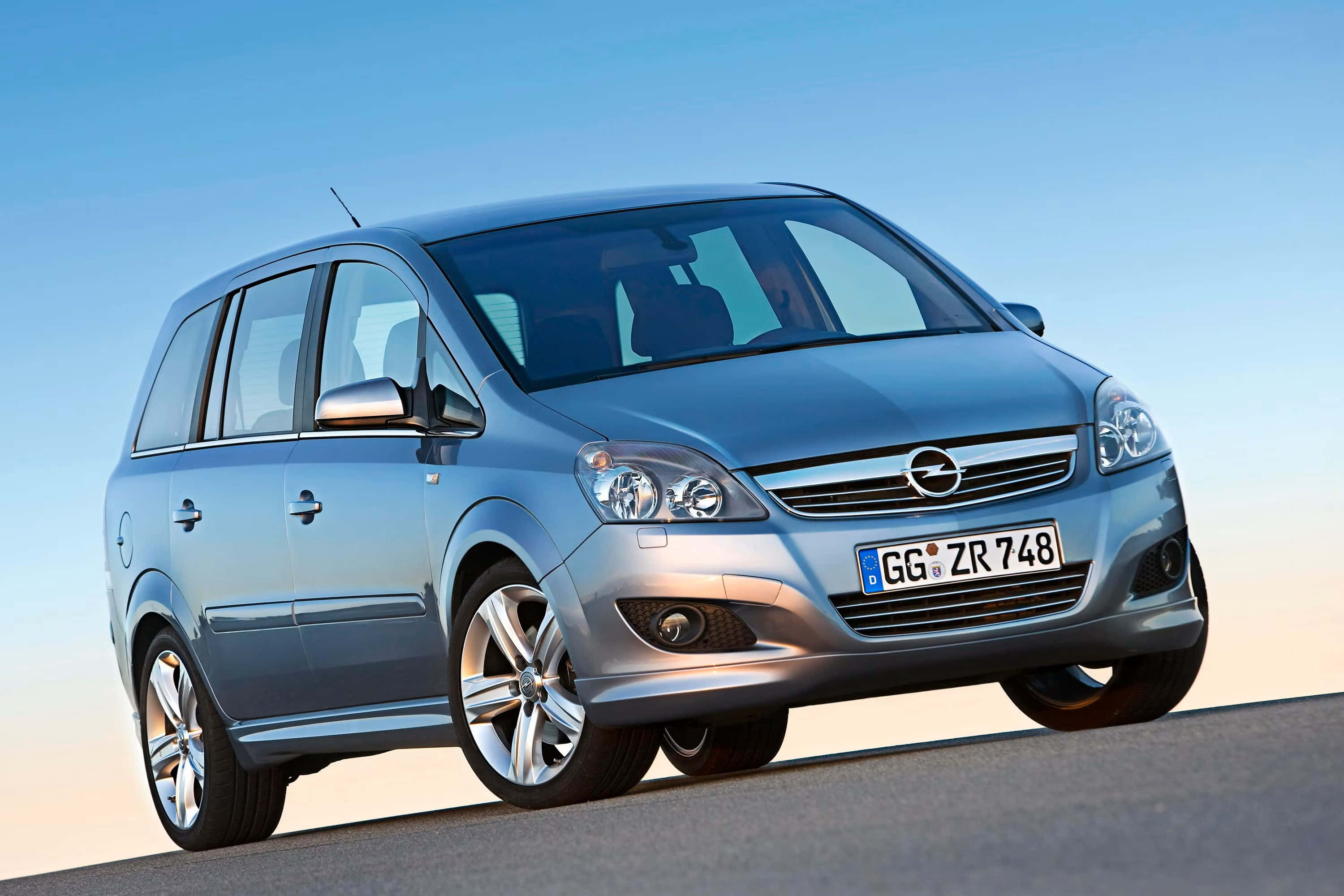 Opel Zafira 桌布 壁紙 — 一輛時尚的銀色歐寶Zafira小型貨車在明亮的日光下，在平坦的道路上閃閃發光，背景是清澈的藍天。