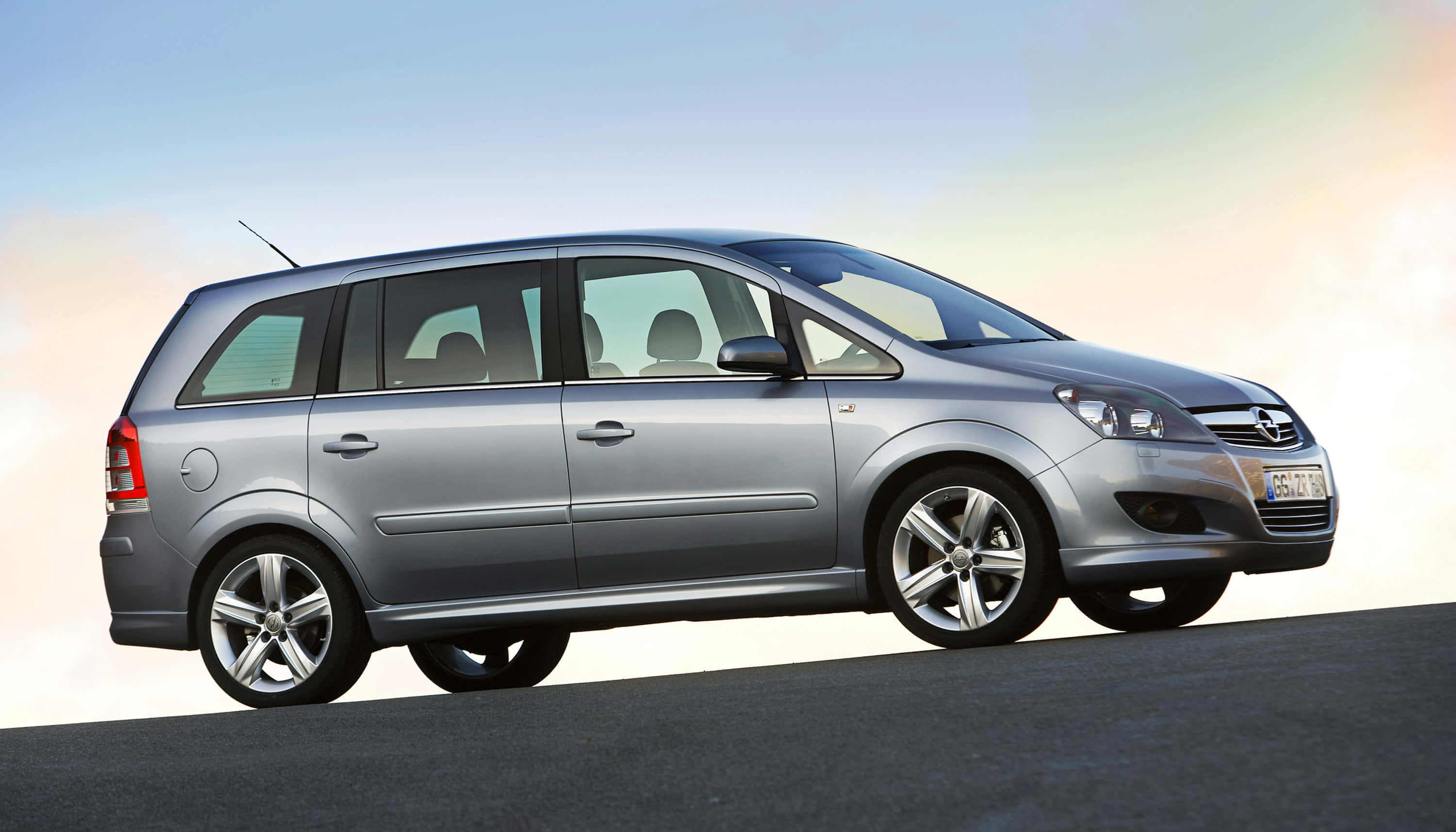Opel Zafira 桌布 壁紙 — 一輛時尚的銀色Opel Zafira旅行車停在瀝青路上，天空呈現柔和漸變色，帶有溫暖的日出色調。