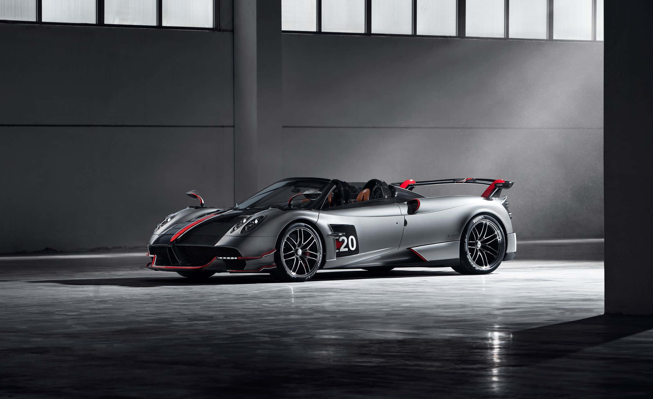 Pagani Huayra Roadster Bc 桌布 壁紙 — 一架時尚的銀色Pagani Huayra Roadster，帶有紅色點綴和20號，停放在極簡工業車庫中，在戲劇性的燈光下。