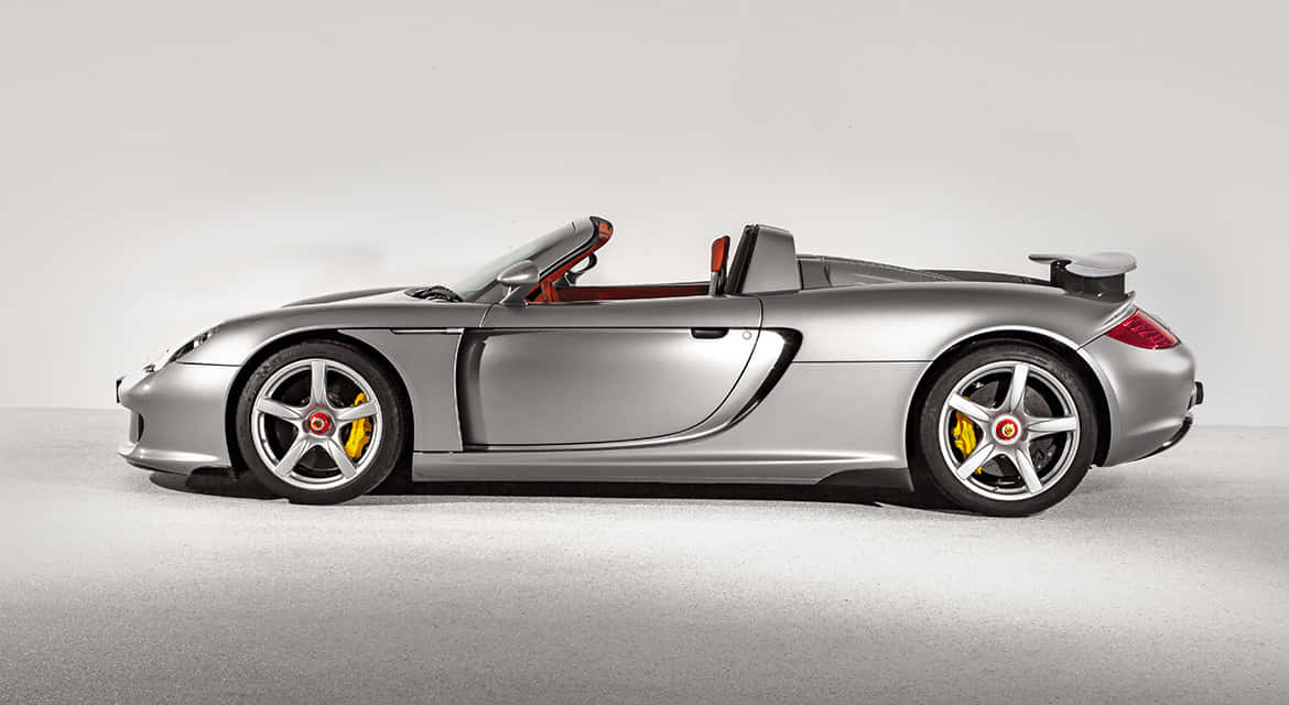 Porsche Carrera Gt 桌布 壁紙 — 一架流線型銀色保時捷Carrera GT開篷跑車，配紅色內飾及黃色制動卡鉗，佇立於簡約工作室場景中。