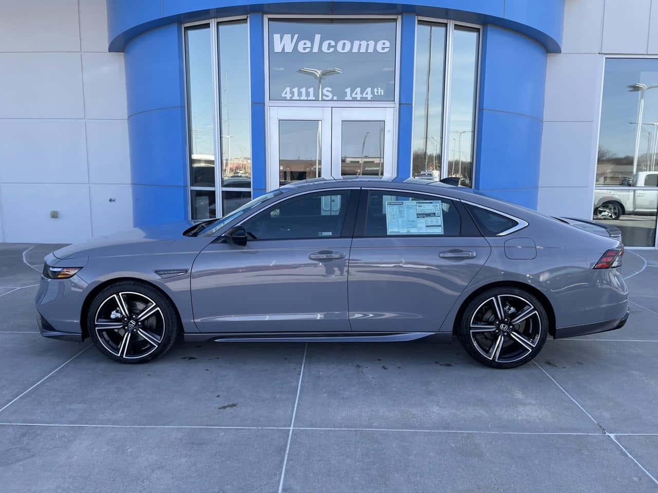 Honda Accord 桌布 壁紙 — 一輛時尚的銀色轎車配黑色輪圈，停在現代化經銷商前，該經銷商有藍色弧形牆壁和玻璃門。