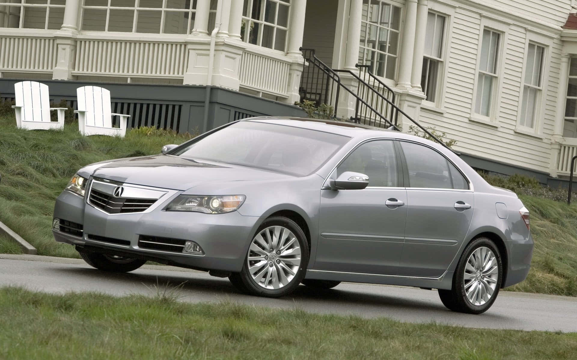Acura Rl 桌布 壁紙 — 一輛時尚的銀色轎車停泊在白色房屋前的鋪砌道路上，房屋前有草坪椅和綠草。