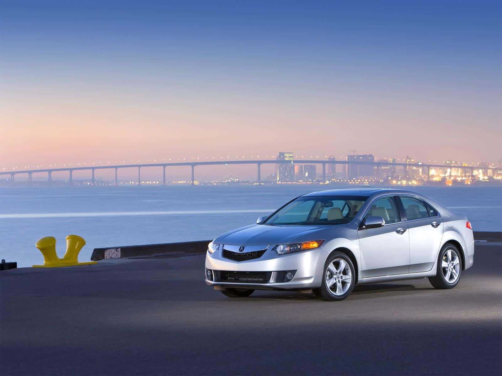 Acura Tsx 桌布 壁紙 — 一輛時尚的銀色轎車停泊在海濱碼頭，暮色中遠方有發光的城市天際線和橋樑。
