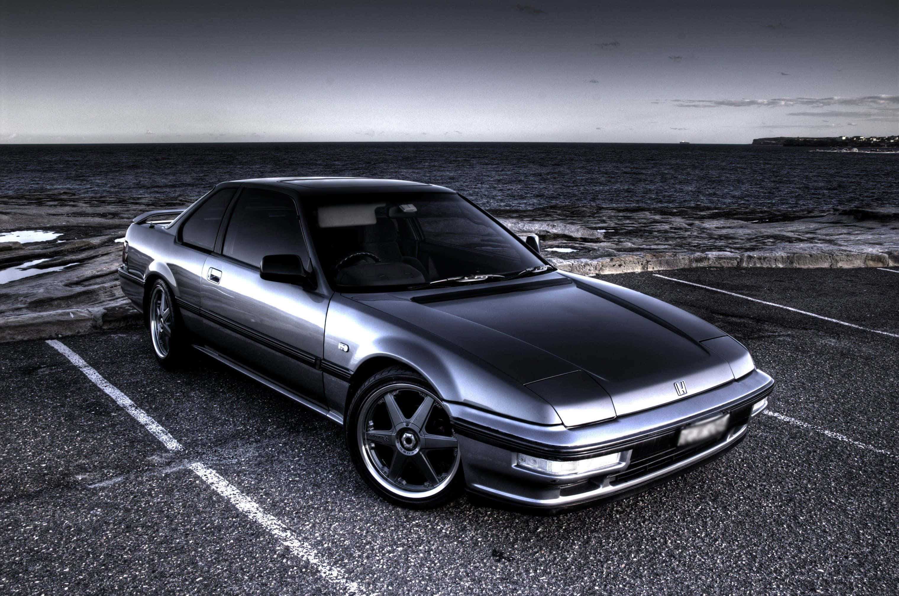 Honda Prelude 桌布 壁紙 — 一架時尚的銀色跑車停泊在沿海的瀝青停車場，背景是海洋和天空。