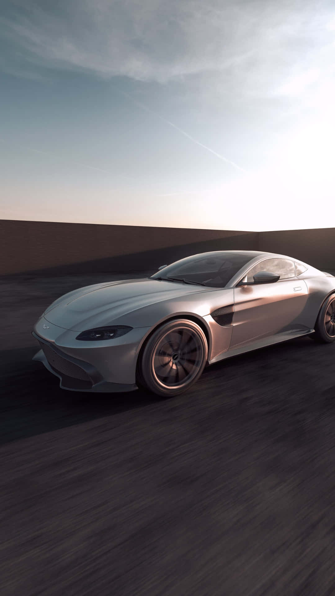 Aston Martin Vantage 桌布 壁紙 — 一輛流線型銀色跑車在昏暗的道路上奔馳，天空是柔和的暮色，雲彩呈條紋狀。