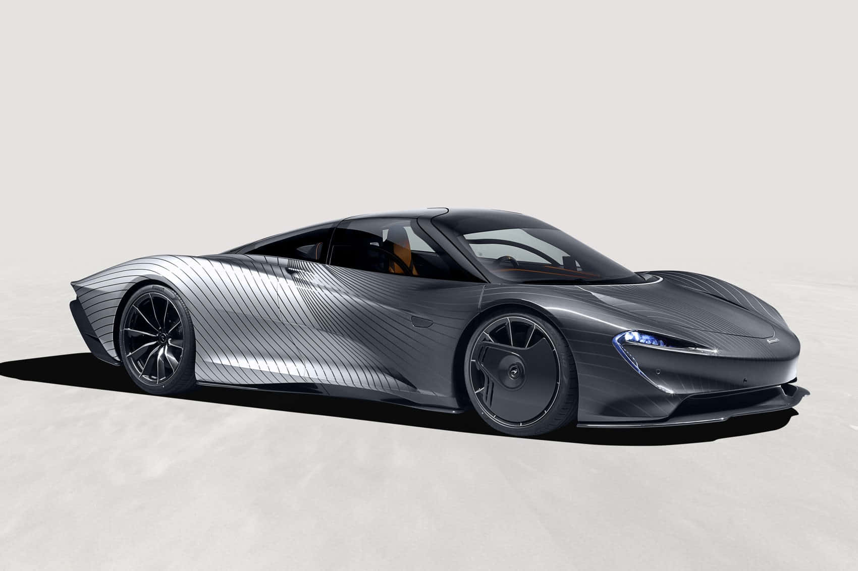 Mclaren Speedtail 桌布 壁紙 — 一輛時尚的銀色跑車，帶有碳纖維細節和發光的藍色車頭燈，矗立在簡約的攝影棚地板上。