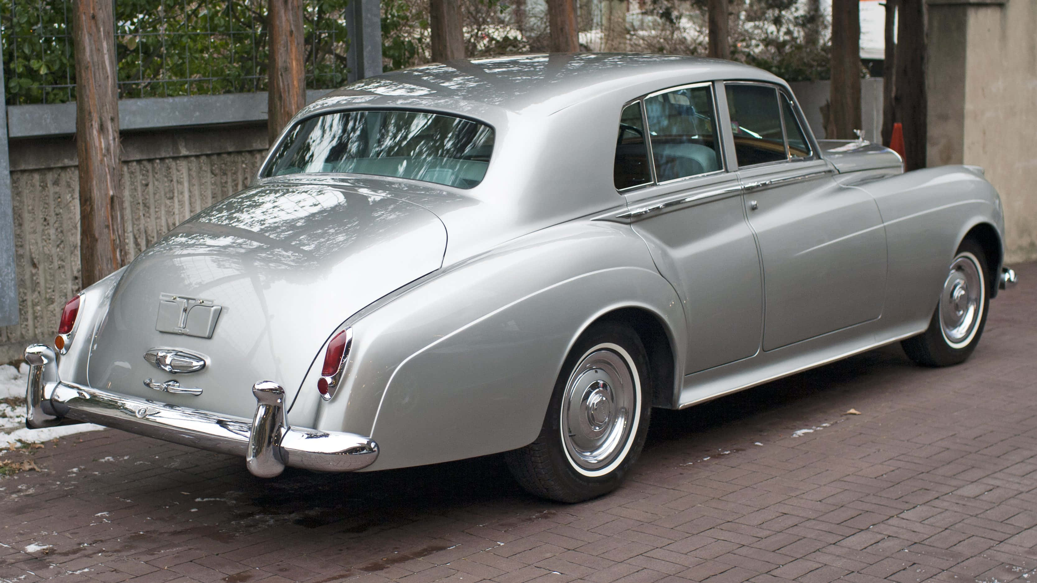 Bentley S2 桌布 壁紙 — 一輛時尚的銀色復古賓利轎車停在磚砌車道上，背景有雪堆和木柵欄。