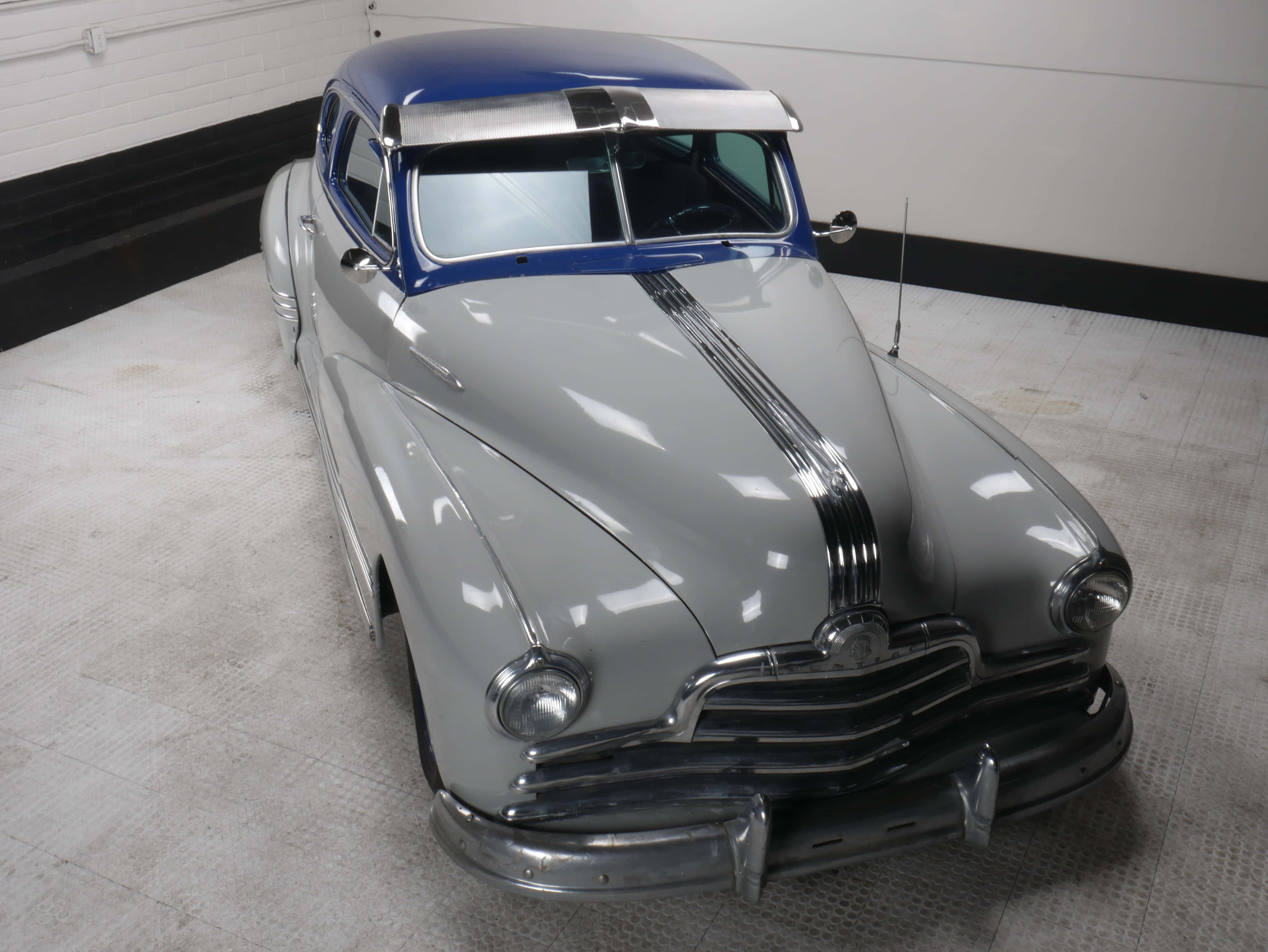 Pontiac Streamliner 桌布 壁紙 — 一輛時尚的銀色復古車，配有藍色車頂和鍍鉻裝飾，在乾淨的車庫中閃閃發光。