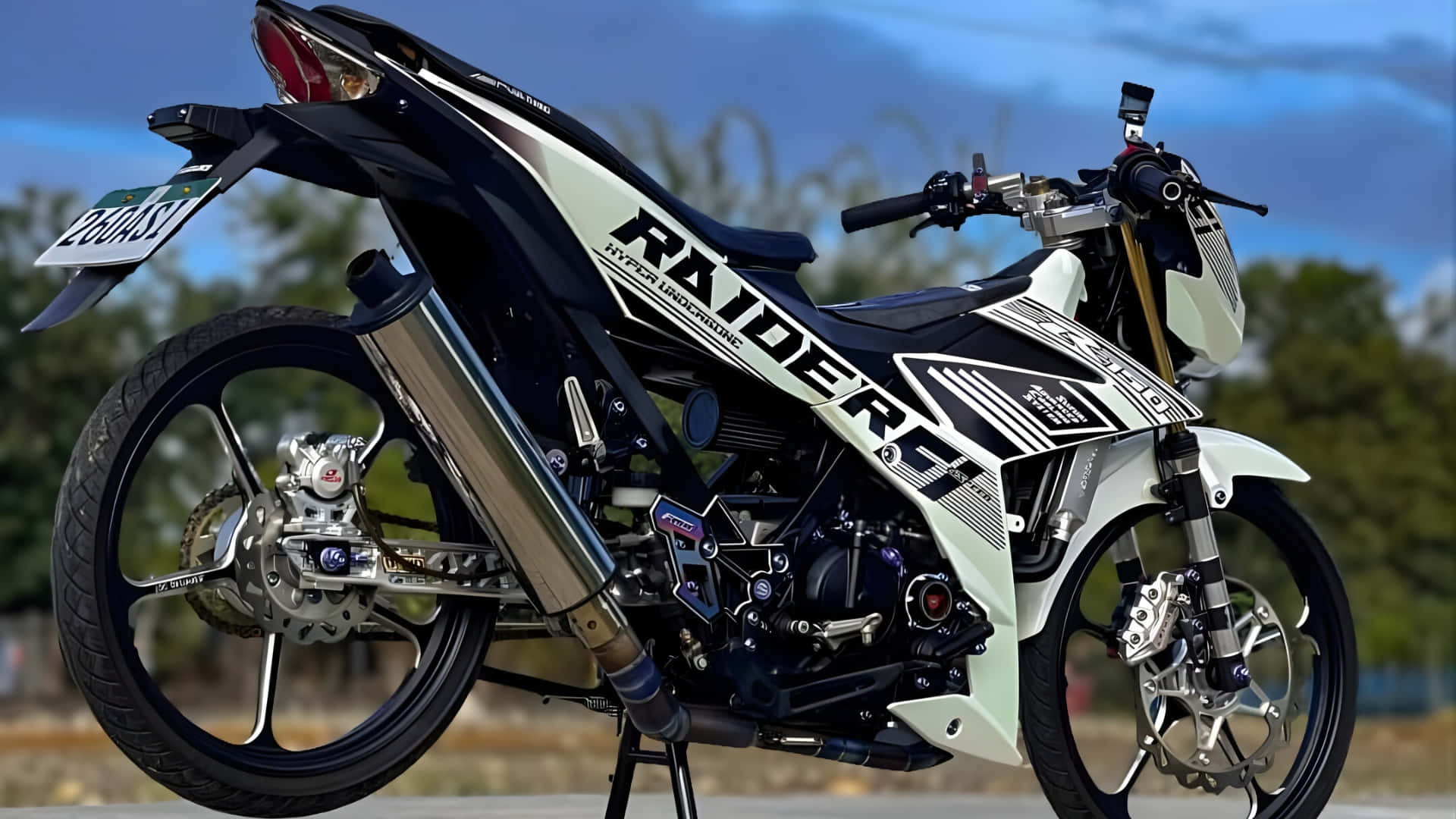  壁紙 — 一架時尚的白色和黑色 Raider 電單車，帶有鍍鉻排氣管，放在支架上，背景是模糊的戶外景色。