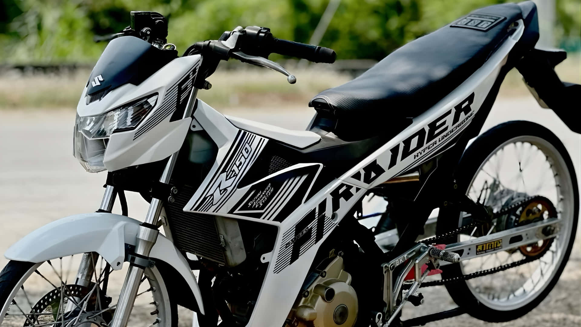  壁紙 — 一架型格黑白 Suzuki 電單車，帶有醒目圖案，停泊在鋪砌路面上，背景有綠化植物。