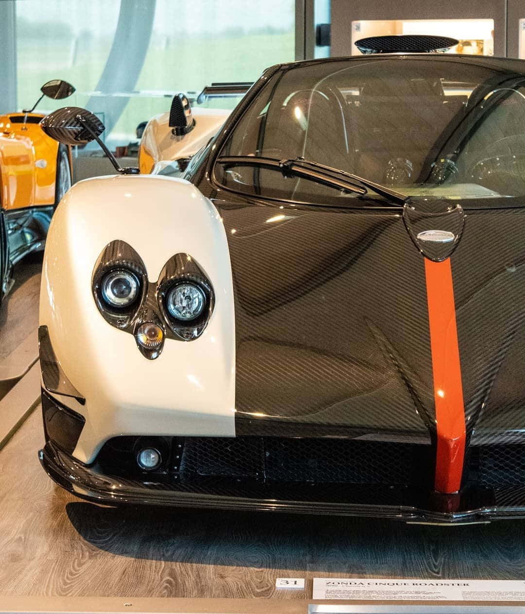 Pagani Zonda C12 Roadster 桌布 壁紙 — 一輛時尚的白色和碳纖維帕加尼Zonda Cinque Roadster，帶有橙色條紋，陳列在豪華車展廳中。