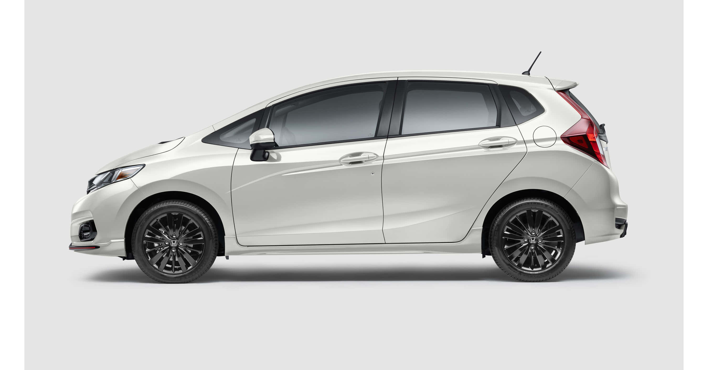 Honda Fit 桌布 壁紙 — 一輛時尚的白色緊湊型掀背車，帶黑色輪圈，側面展示在純灰色工作室背景前。
