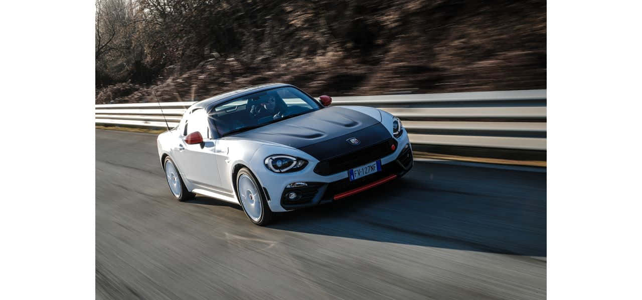 Fiat 124 Spider 桌布 壁紙 — 一架時尚的白色Fiat 124 Spider在蜿蜒的道路上疾馳，帶有動態模糊和岩石山坡背景。