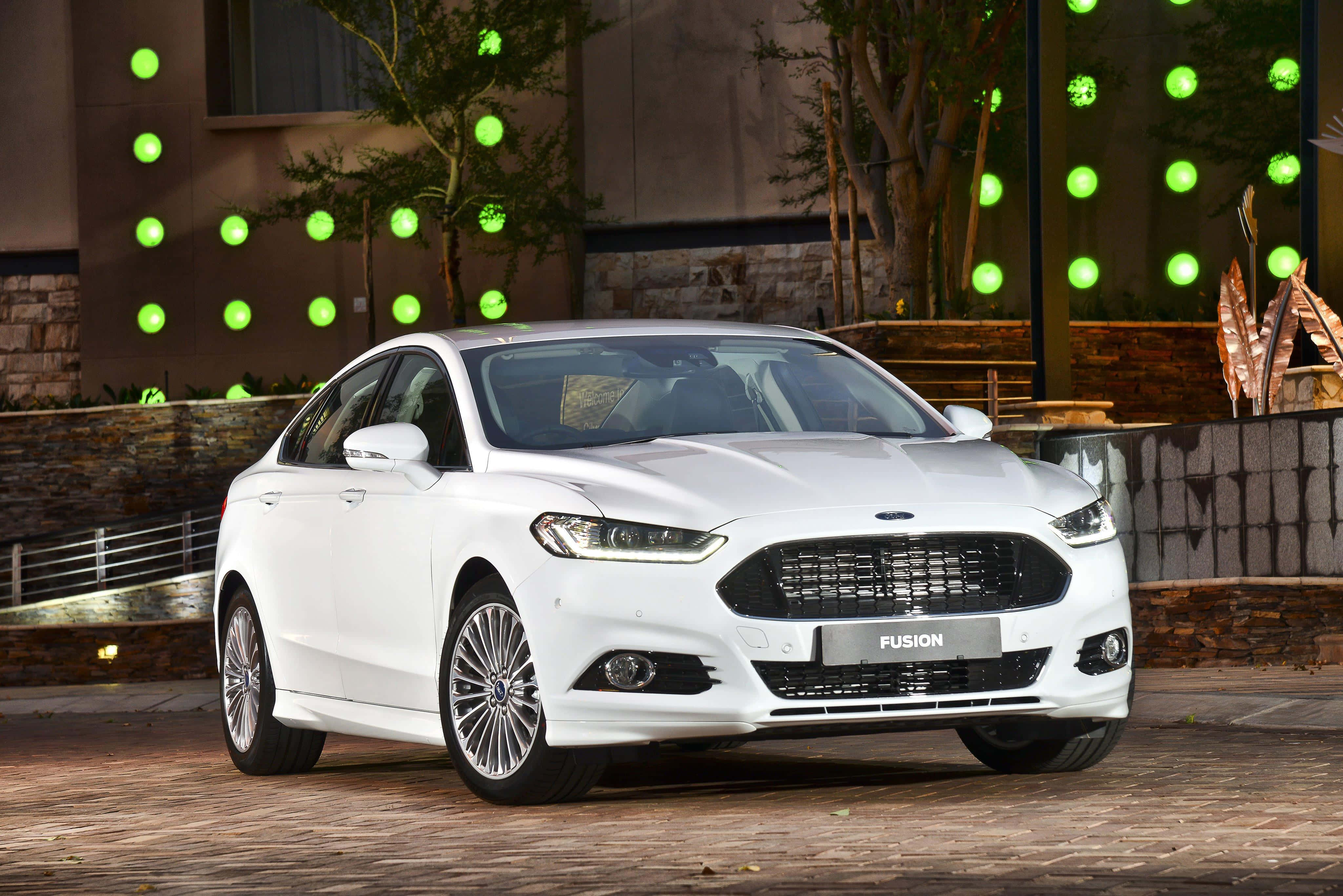Ford Fusion 桌布 壁紙 — 一輛時尚的白色福特Fusion轎車在環境燈光下閃閃發光，背景是裝飾著發光綠色球體的現代建築。