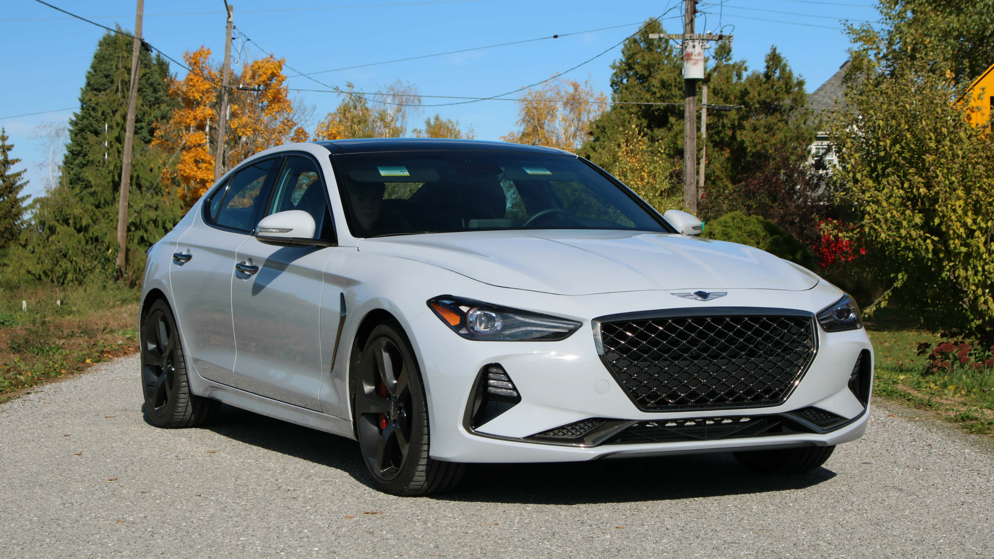 Genesis G70 桌布 壁紙 — 一架時尚的白色Genesis G70運動轎車停在碎石路上，周圍是秋天的樹木，天空清澈湛藍。